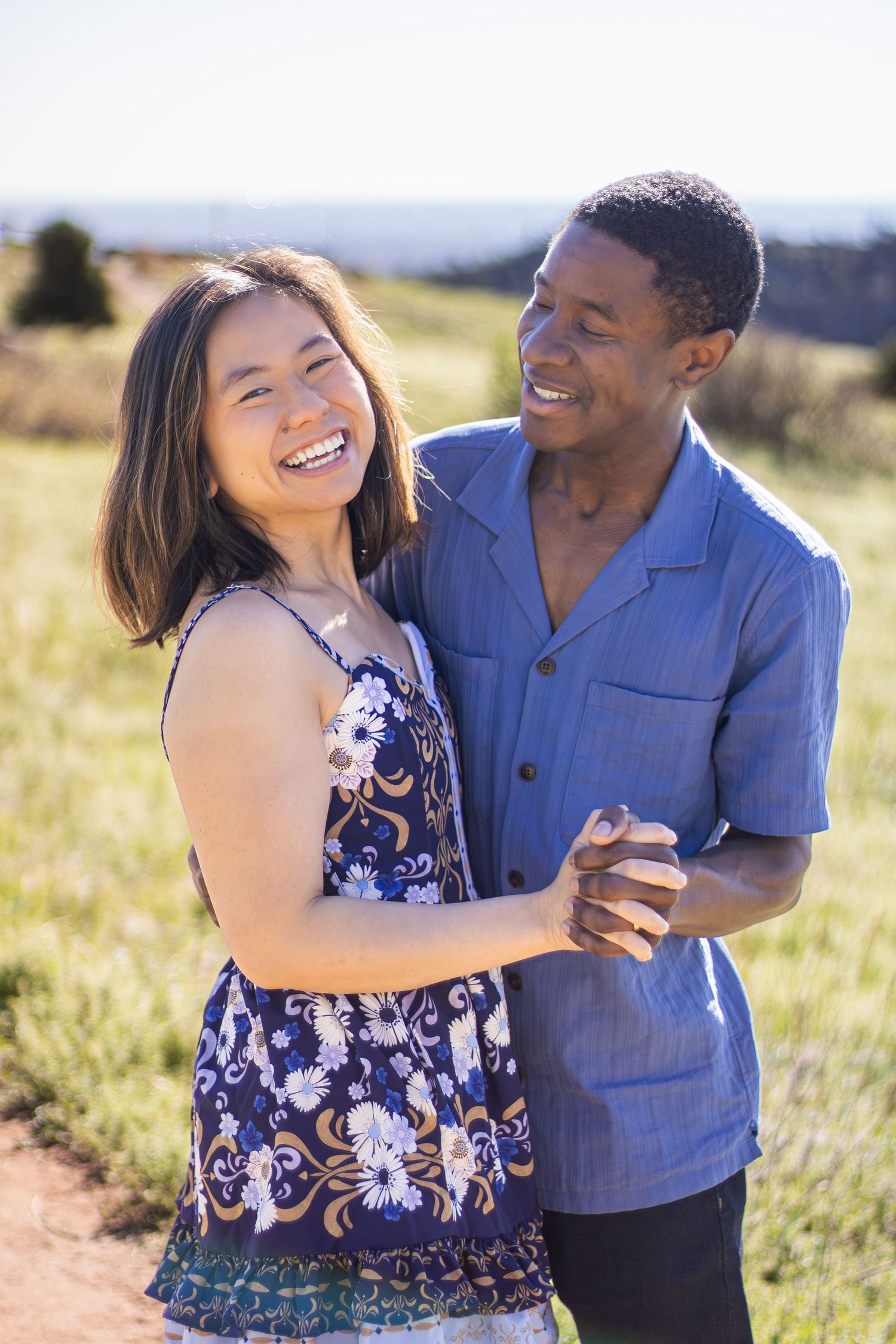 A couple shares joyful moments together in a sunlit field wearing blue and floral outfits.