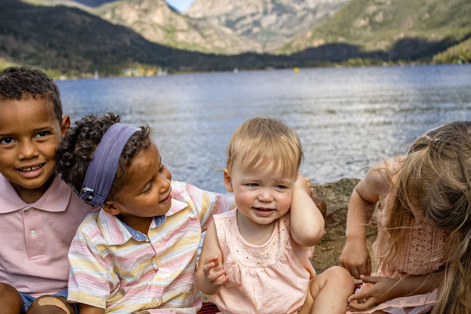 People gathered on a rocky shoreline with mountains and a serene lake creating a beautiful outdoor setting.
