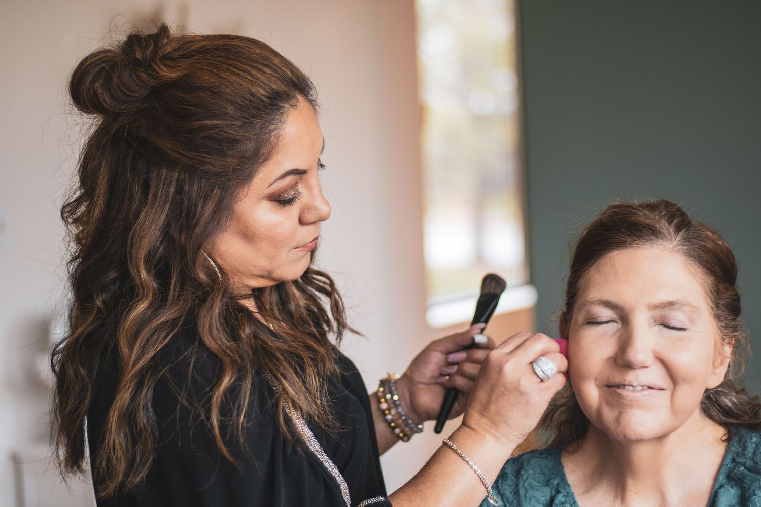 Professional makeup artist applies cosmetics to model during beauty session with soft lighting and blurred background.