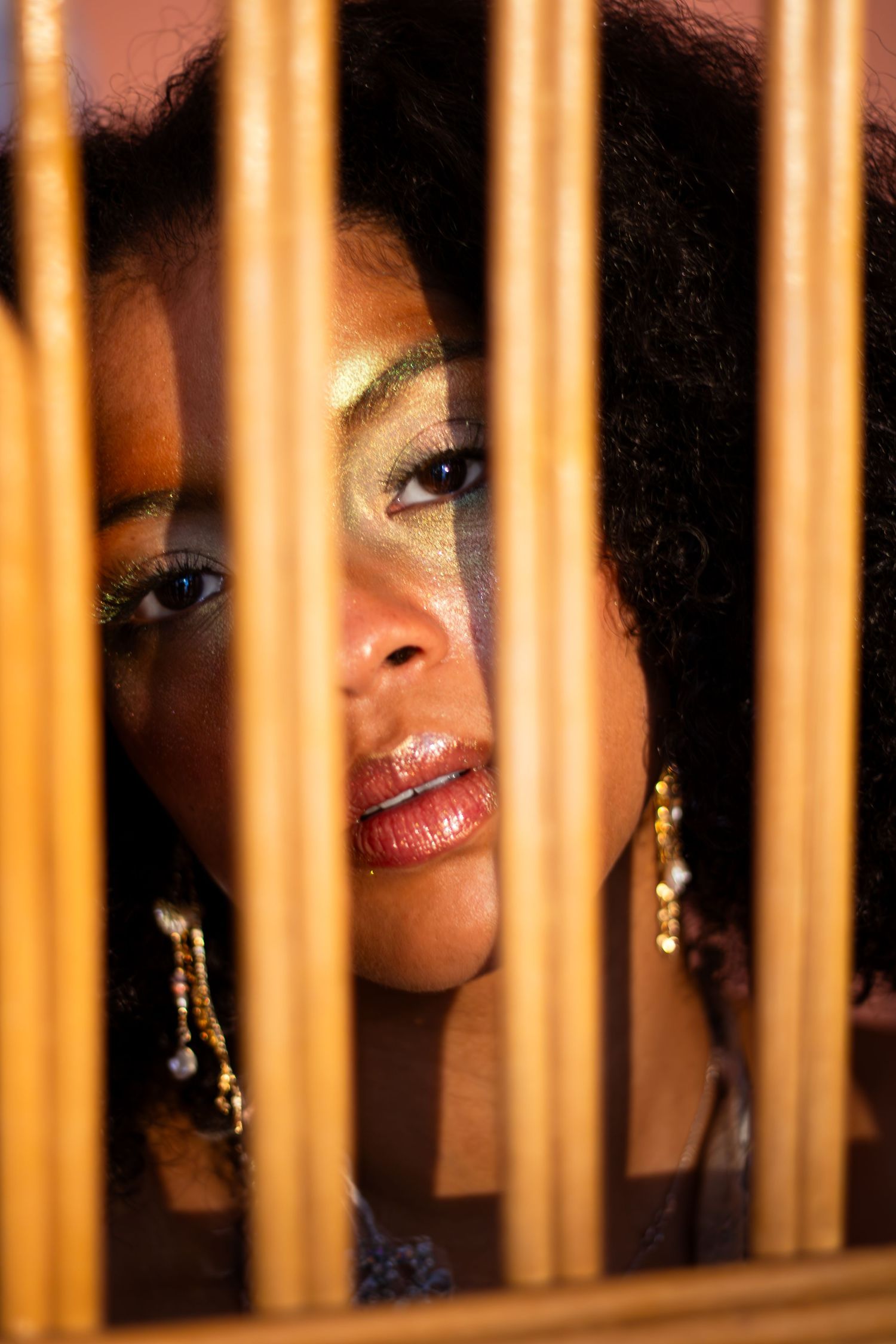 Artistic portrait through golden bars creating a dramatic lighting effect.