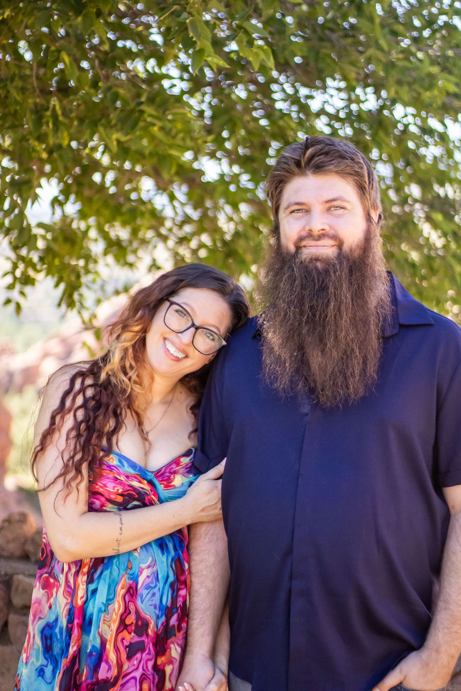 A couple shares a joyful moment outdoors, with her wearing a colorful floral dress and him in a navy shirt.