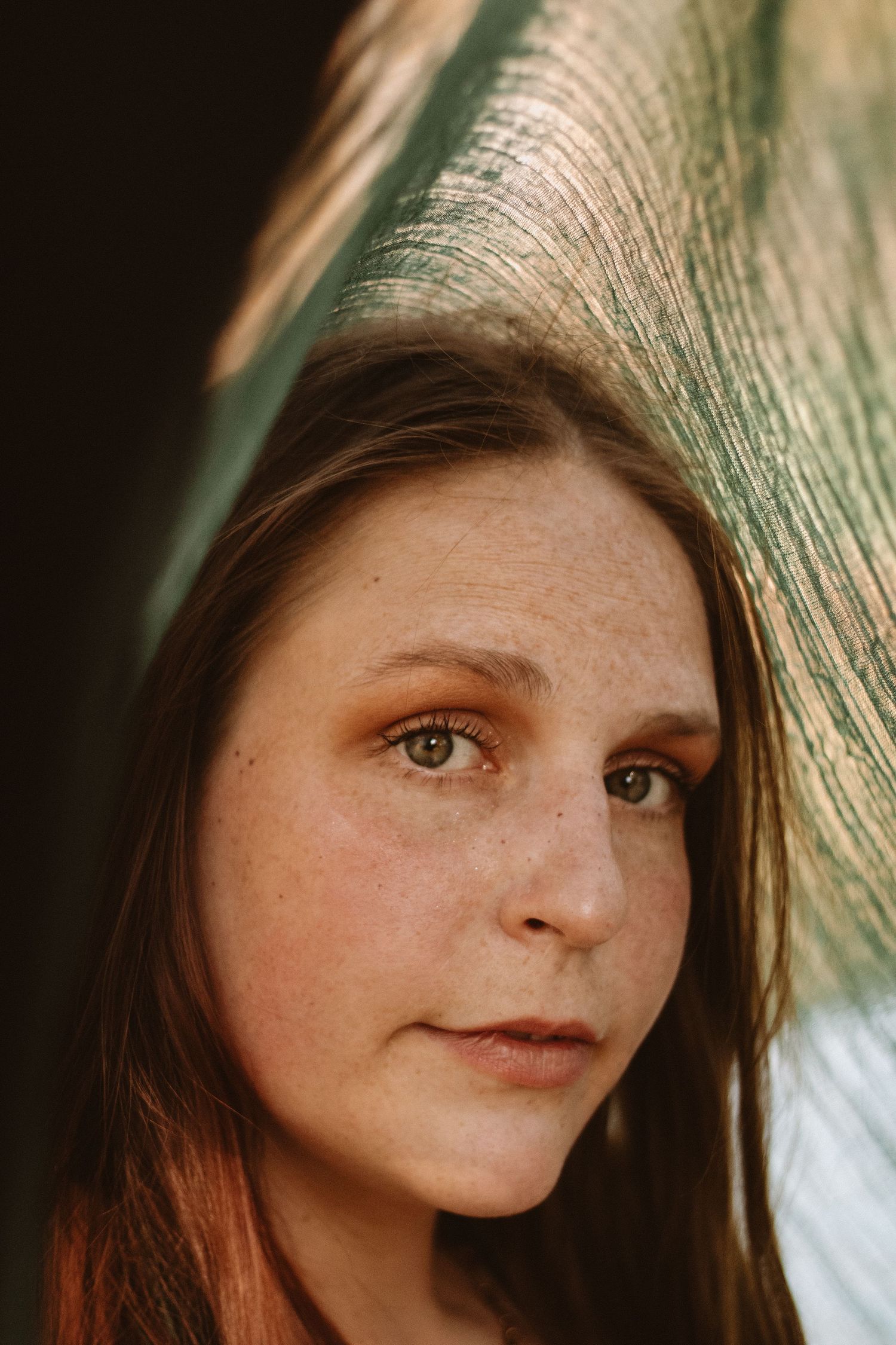 Close-up portrait with warm lighting and a peacock feather, highlighting natural makeup and soft features.