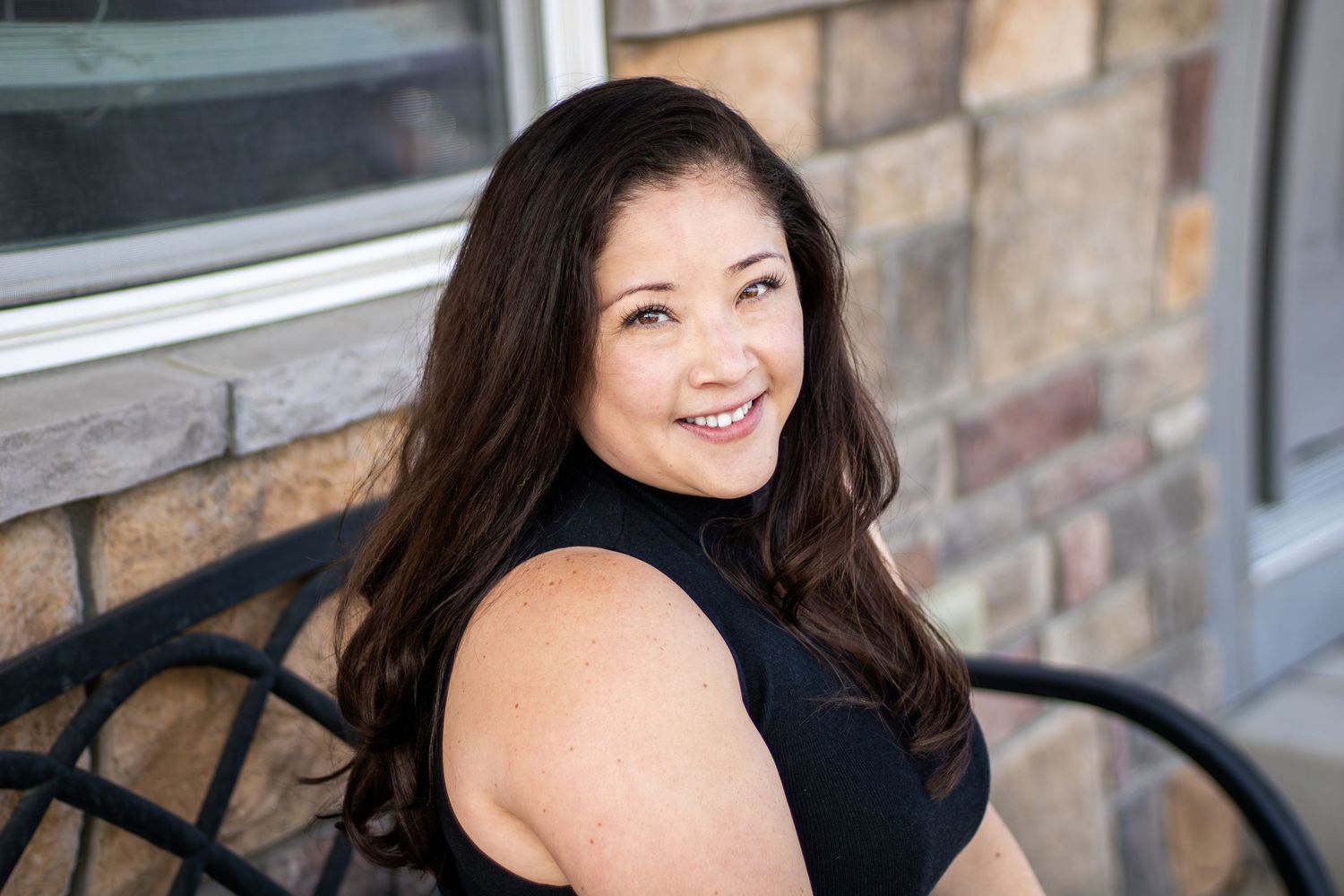 Professional headshot portraits of a woman in a black top against a rustic brick wall background.