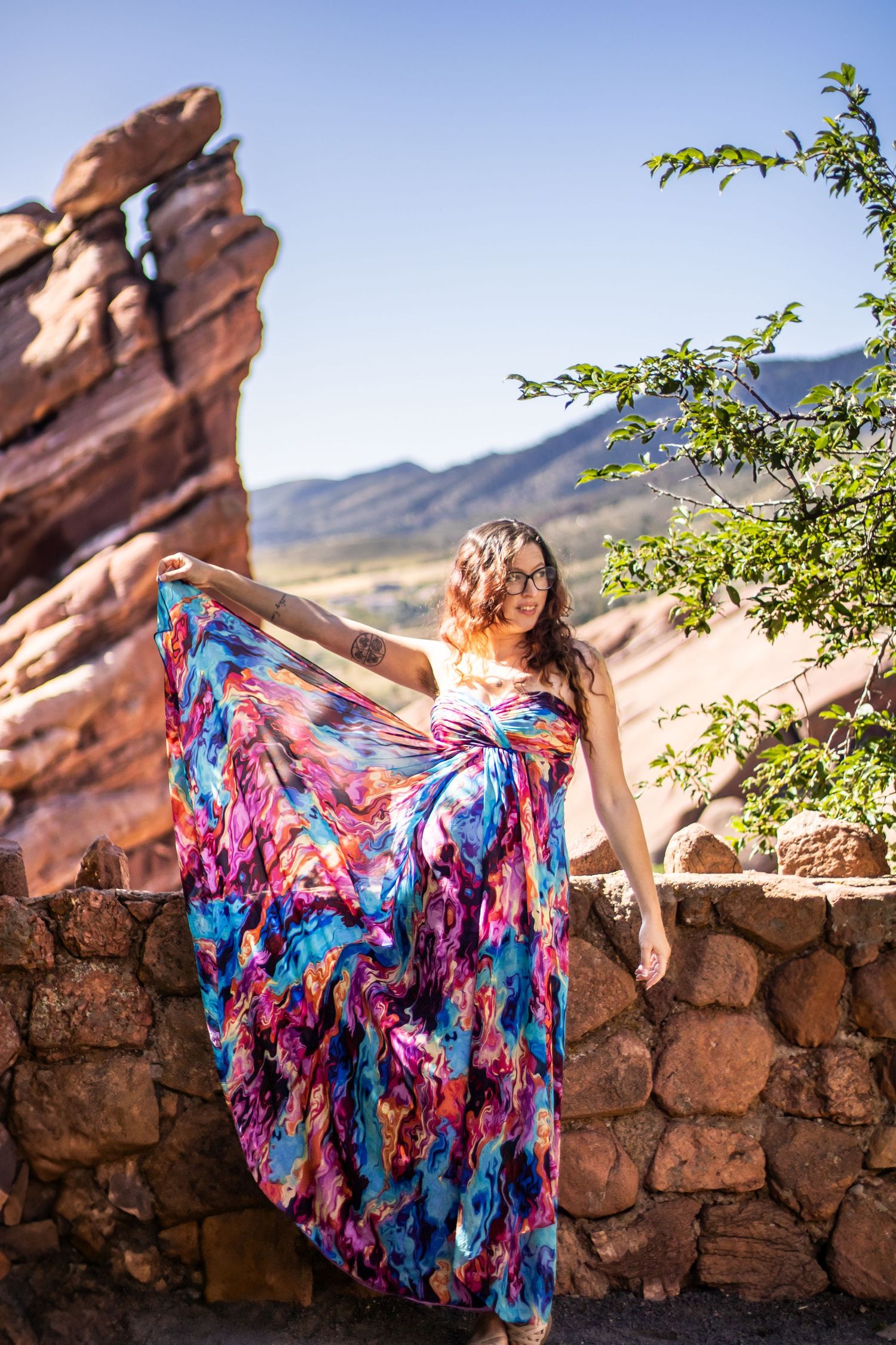A flowing floral dress billows dramatically against red rock formations and desert landscape at sunset.