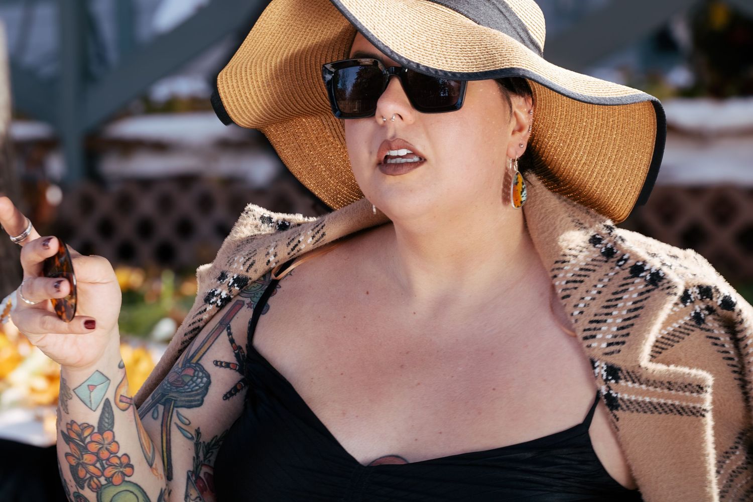 Fashionable person in black dress and wide brim sun hat with sunglasses enjoying outdoor dining.