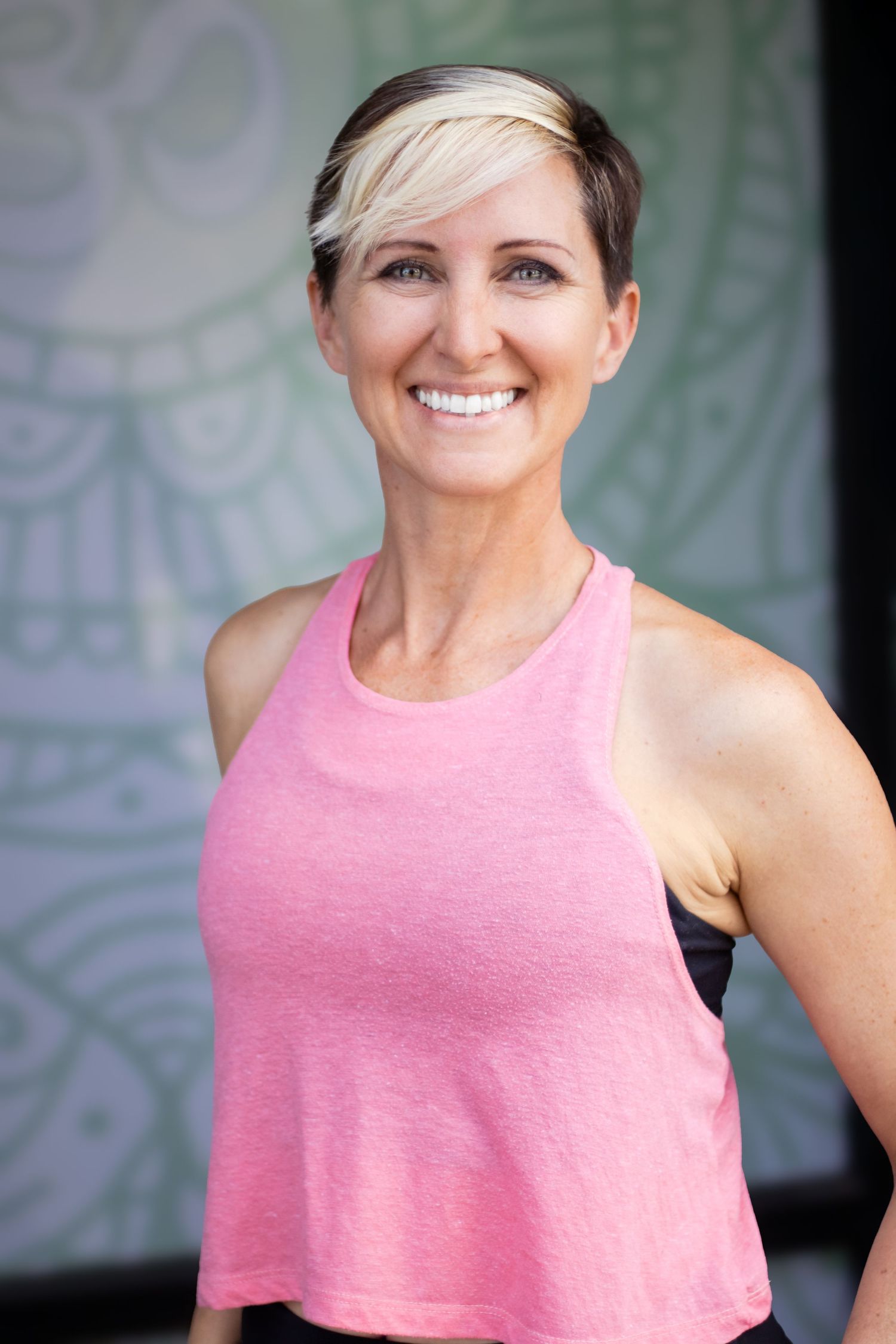 Close-up portrait of someone in a pink sleeveless top with short hair against a light background.