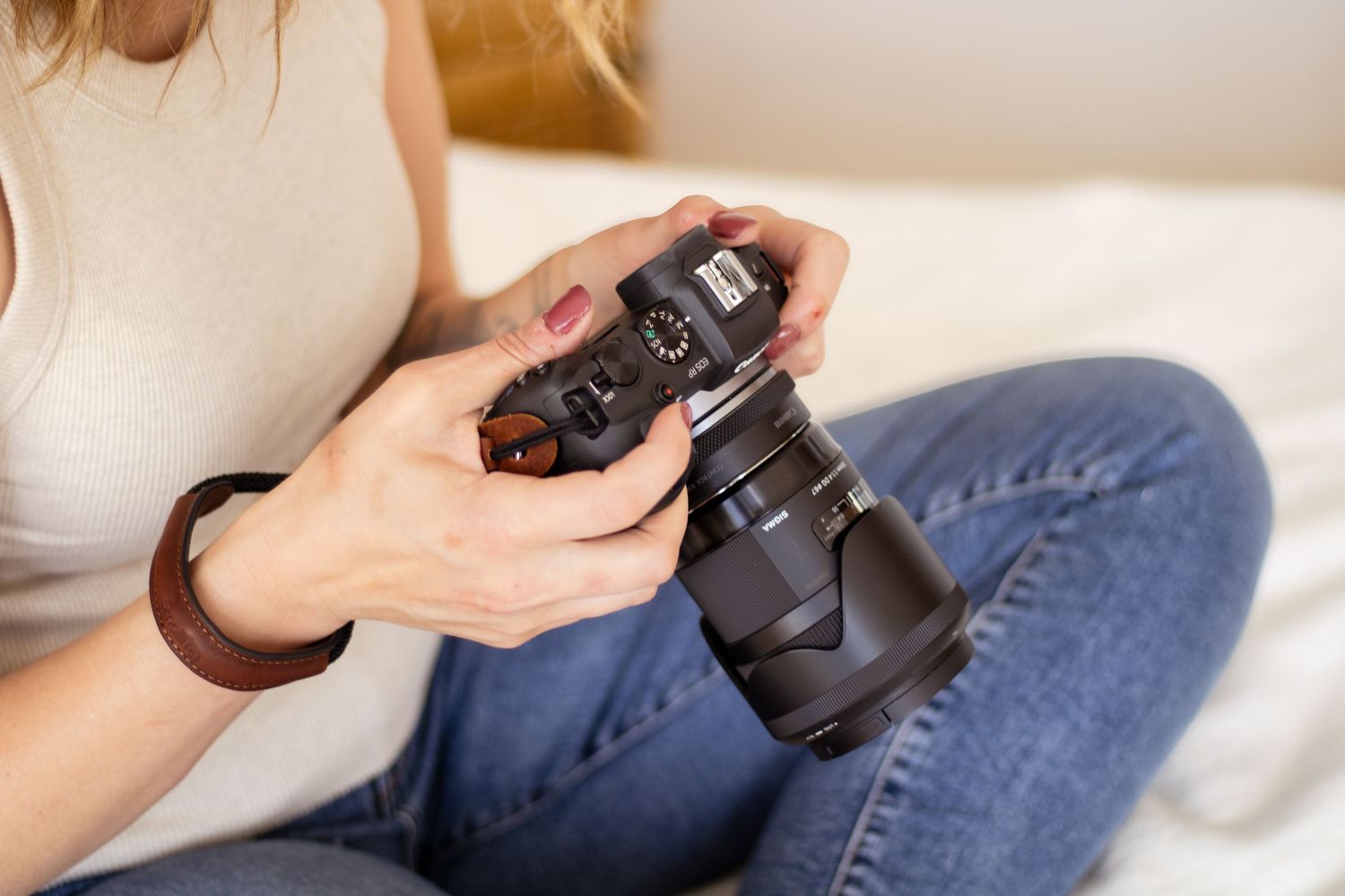 Close-up view of hands holding a professional DSLR camera with large lens while sitting in casual attire.