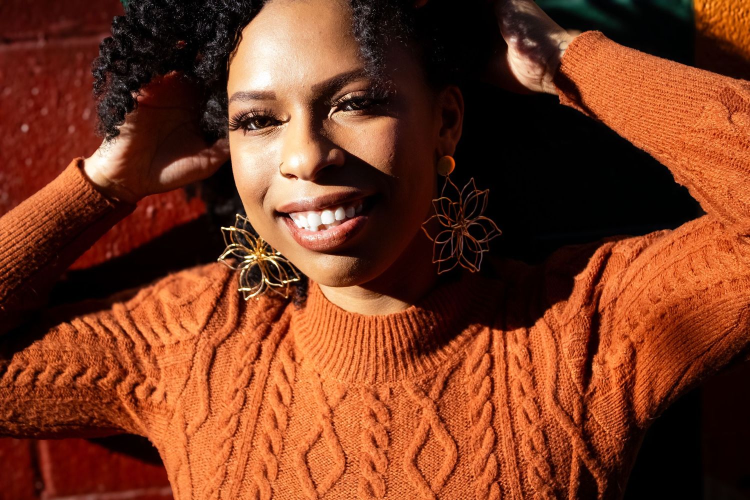 Person wearing a cozy orange cable knit sweater poses against an orange background in warm lighting.