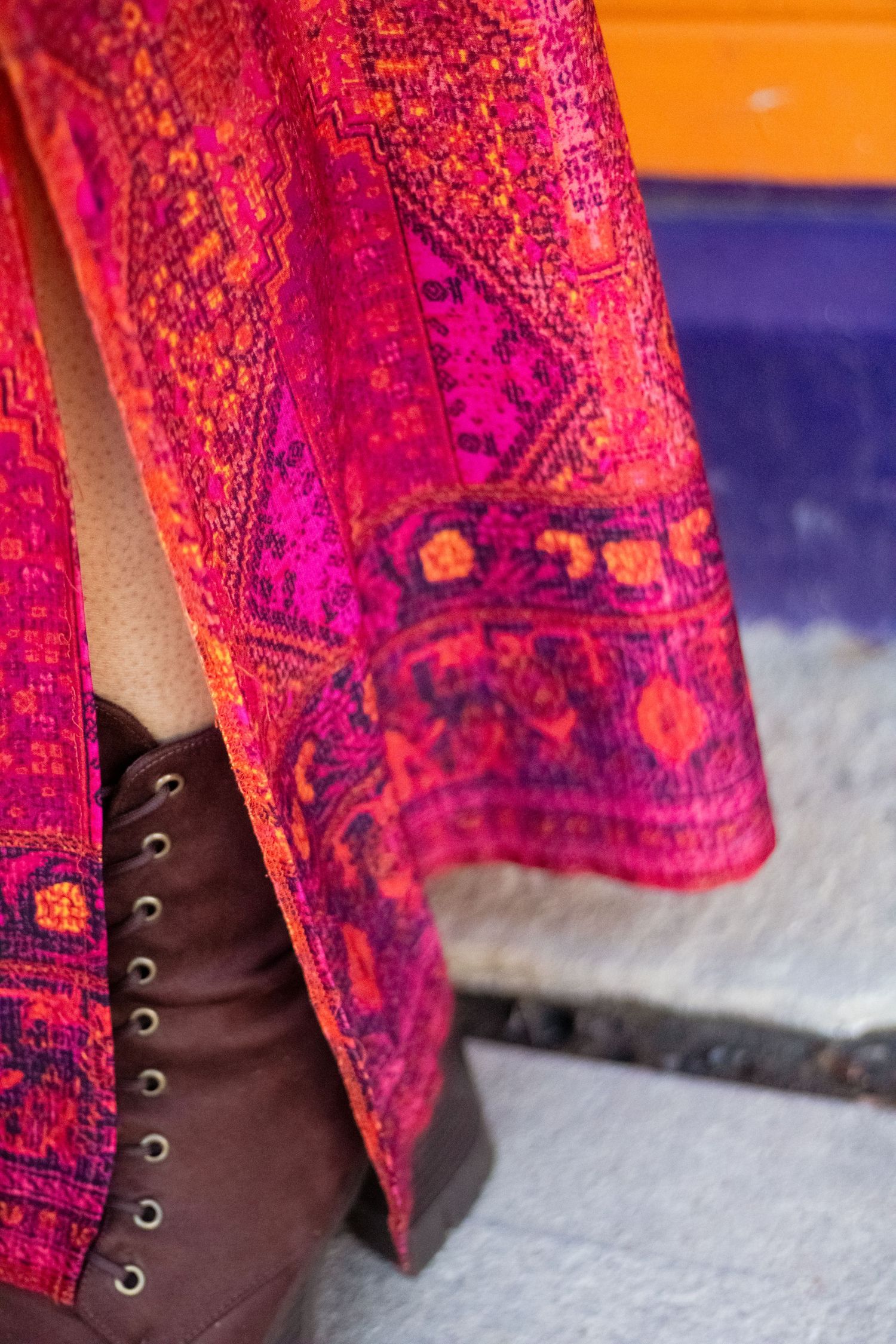 Close-up view of brown leather boots peeking out from under a vibrant pink and purple patterned dress.