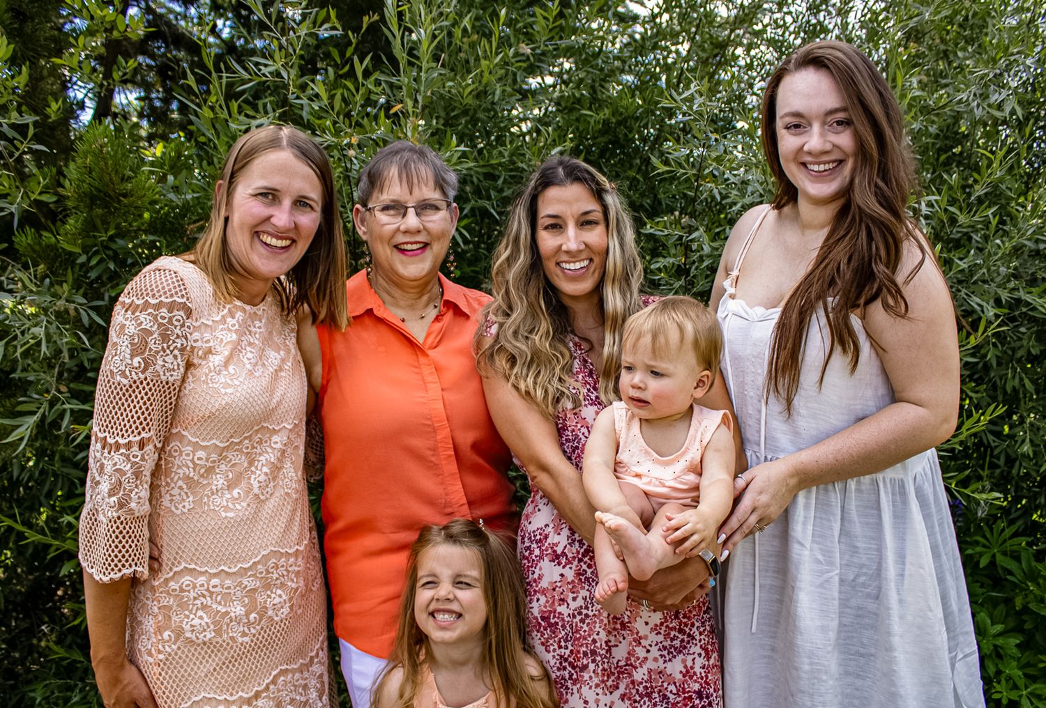 A group photo taken outdoors with everyone wearing coordinated pink and orange outfits against a green backdrop.