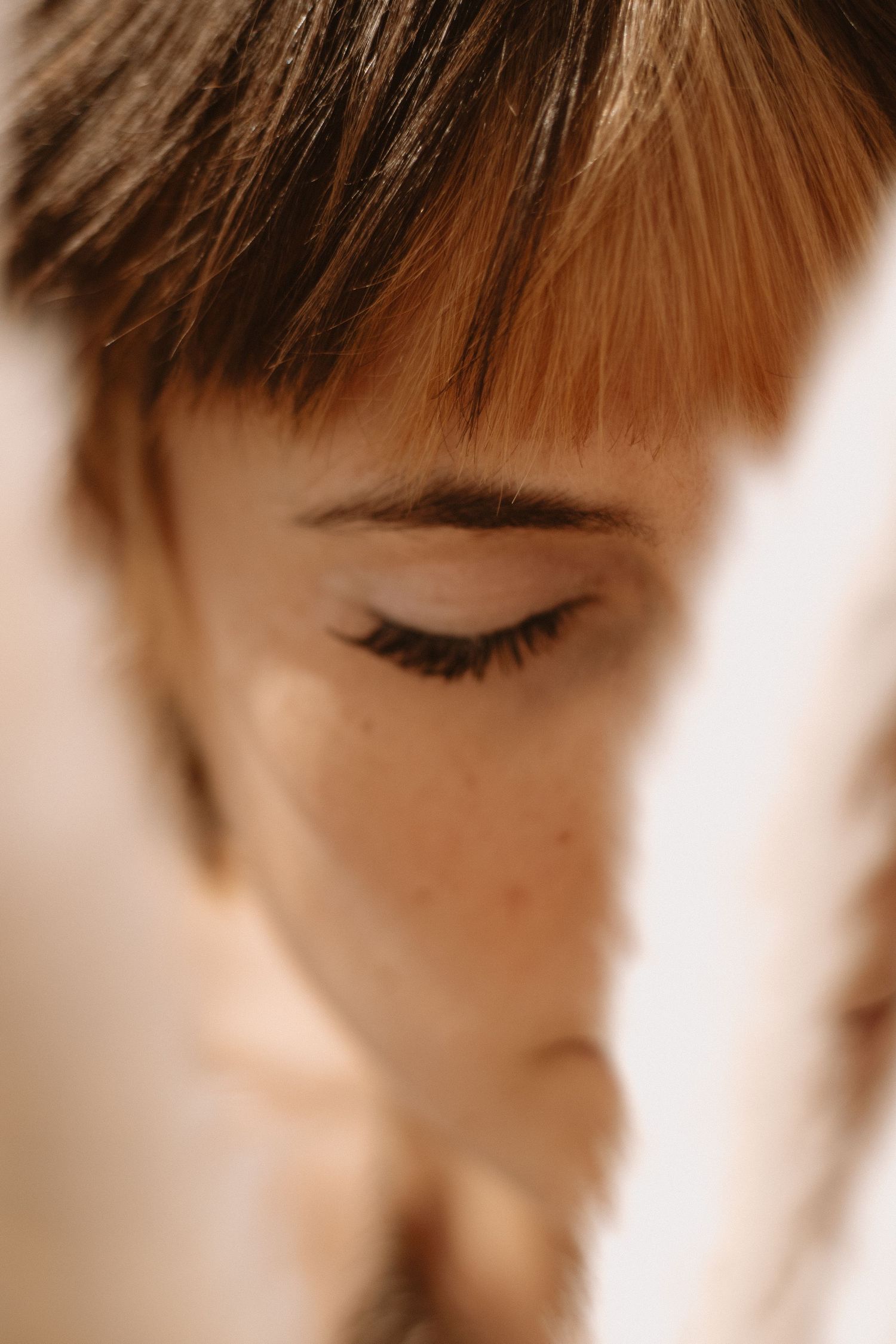 Close-up macro shot of closed eye with long eyelashes and brown hair bangs in soft focus.