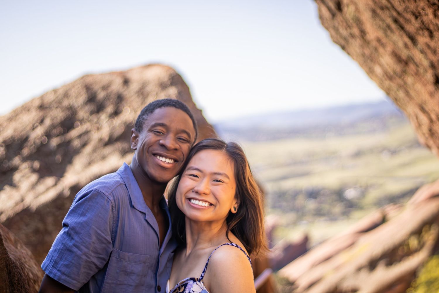 Couple laughing and embracing during a golden hour photoshoot in a desert landscape with rock formations.