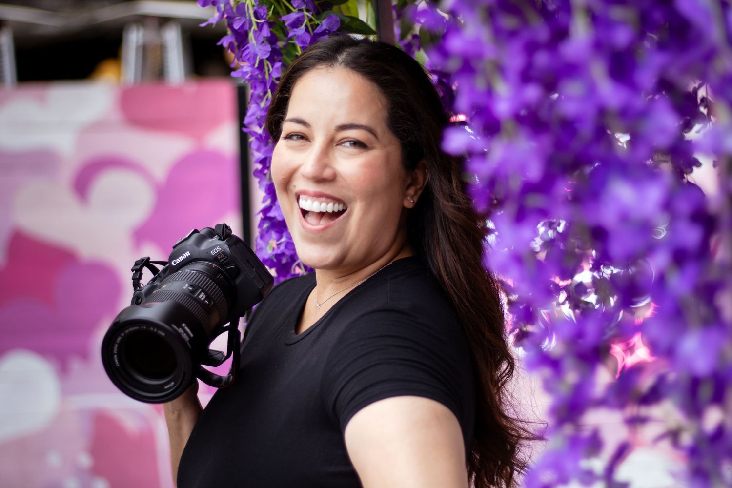 A person in black clothing poses against a vibrant purple floral background during a photography session.