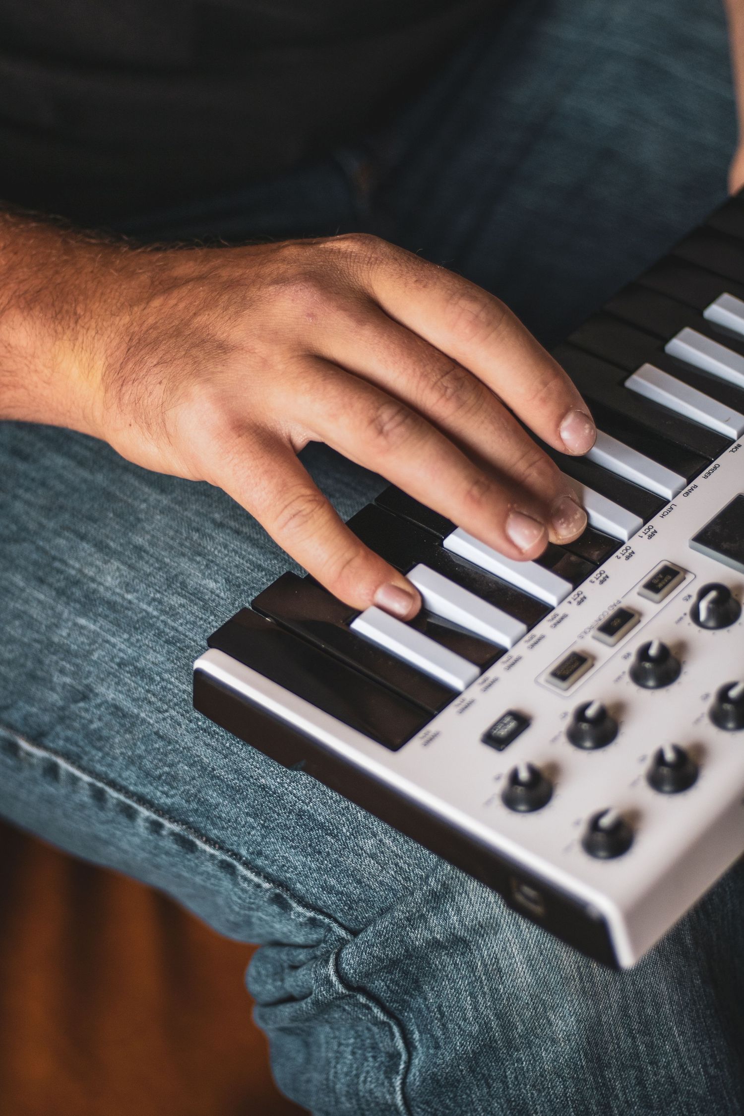 Close-up view of hands playing on a MIDI keyboard controller with black and white keys and control knobs.