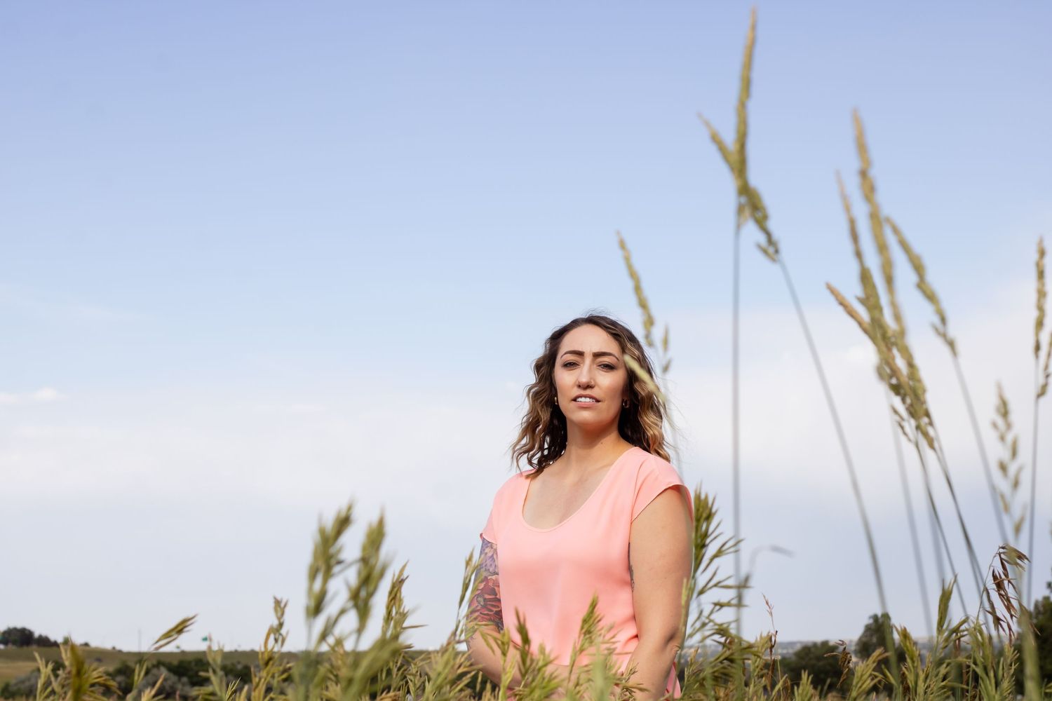 Someone meditates peacefully in a pink tank top among tall grass against a bright blue sky.
