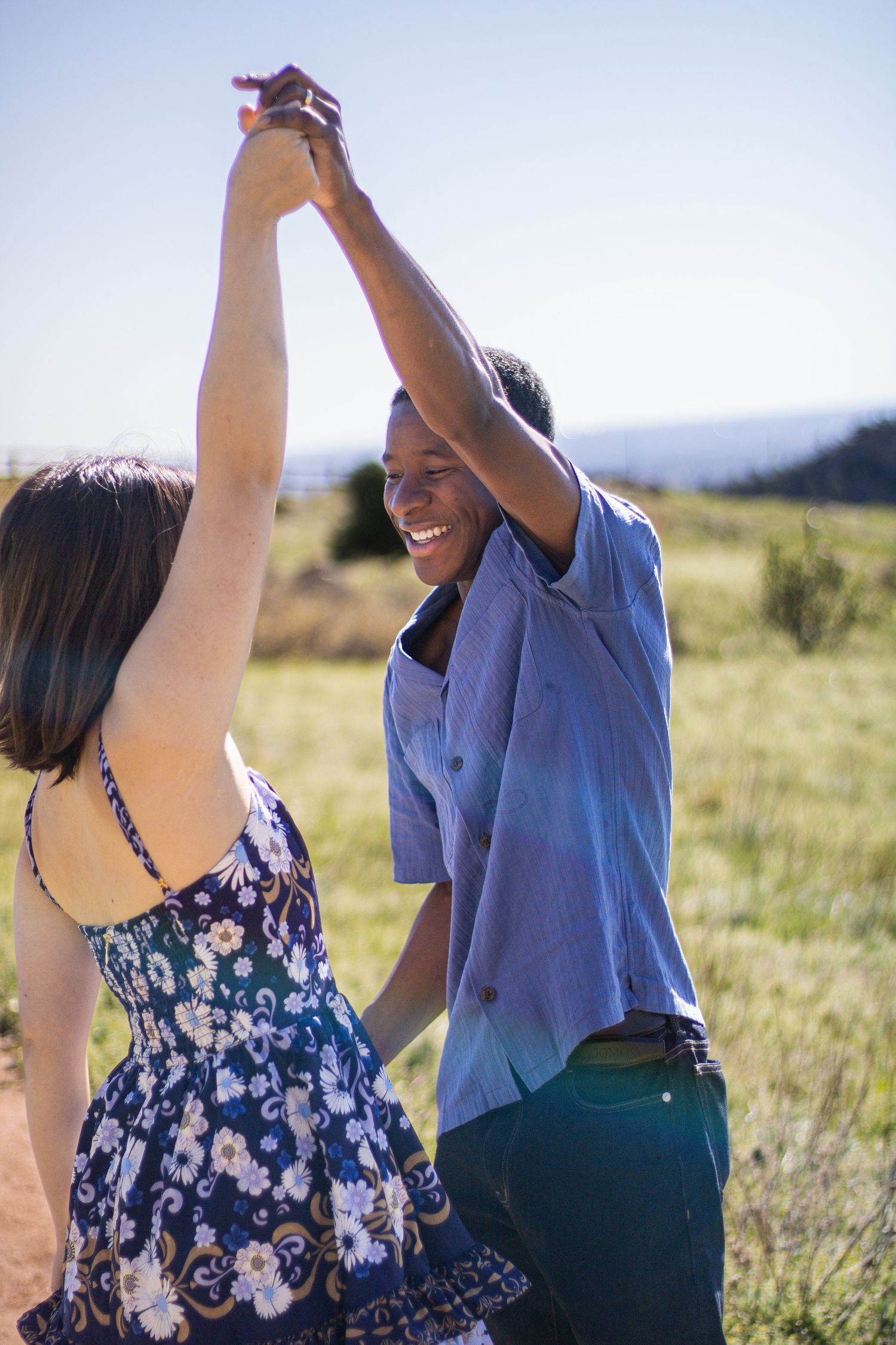 A couple dances together in a sunlit meadow wearing casual summer attire.