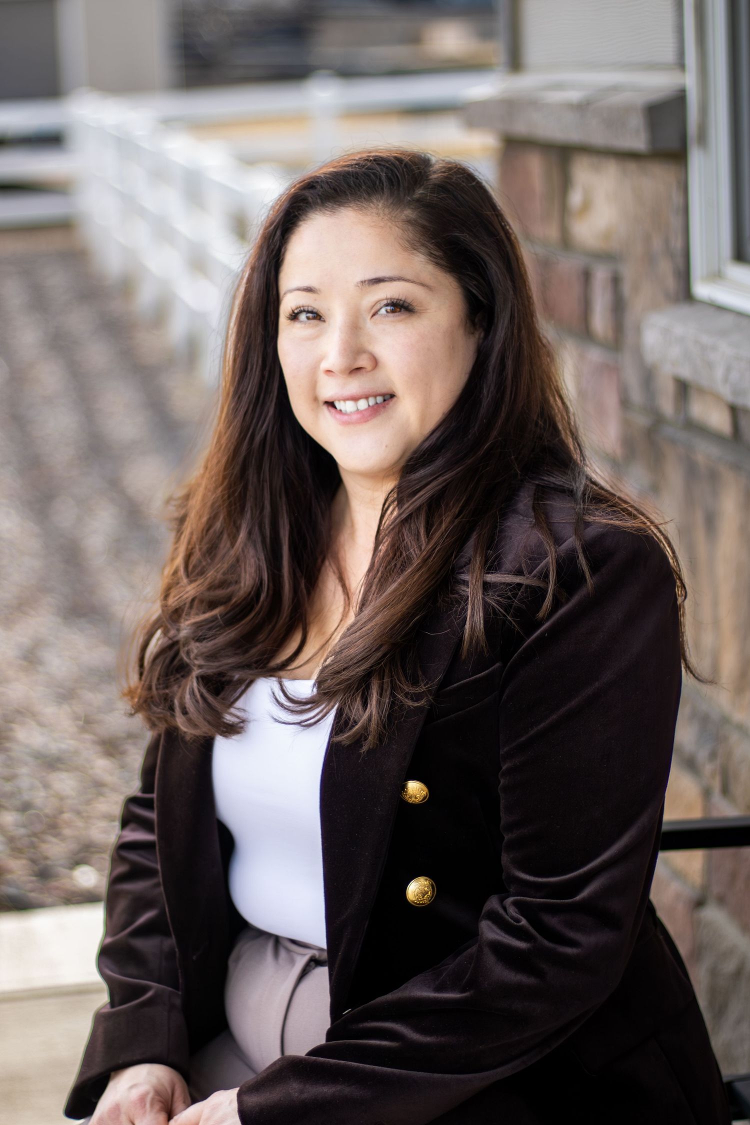 Woman in black blazer and white shirt poses for professional headshots against stone wall background.