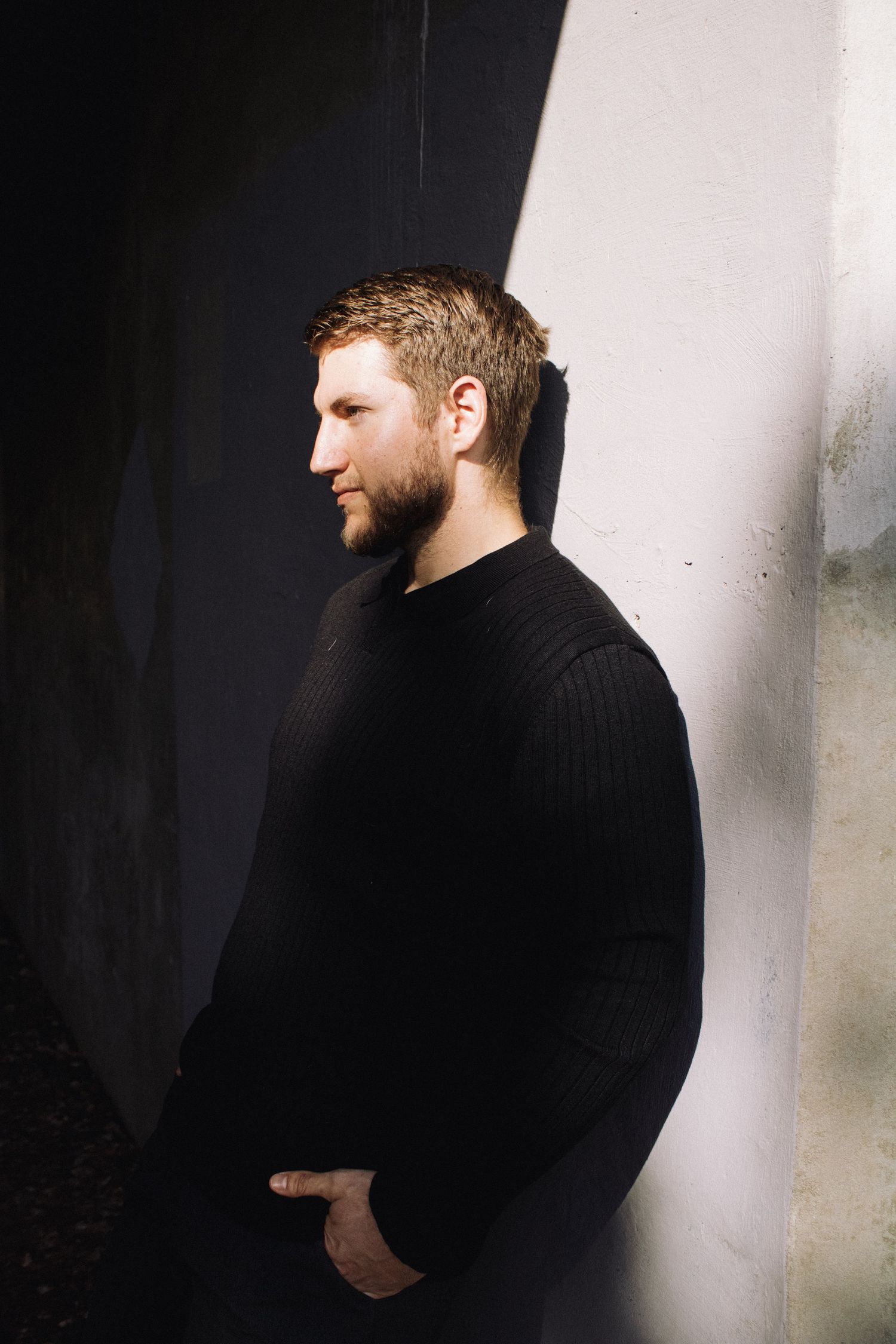 A person wearing a black turtleneck sweater is shown in profile against a white background in a moody portrait series.