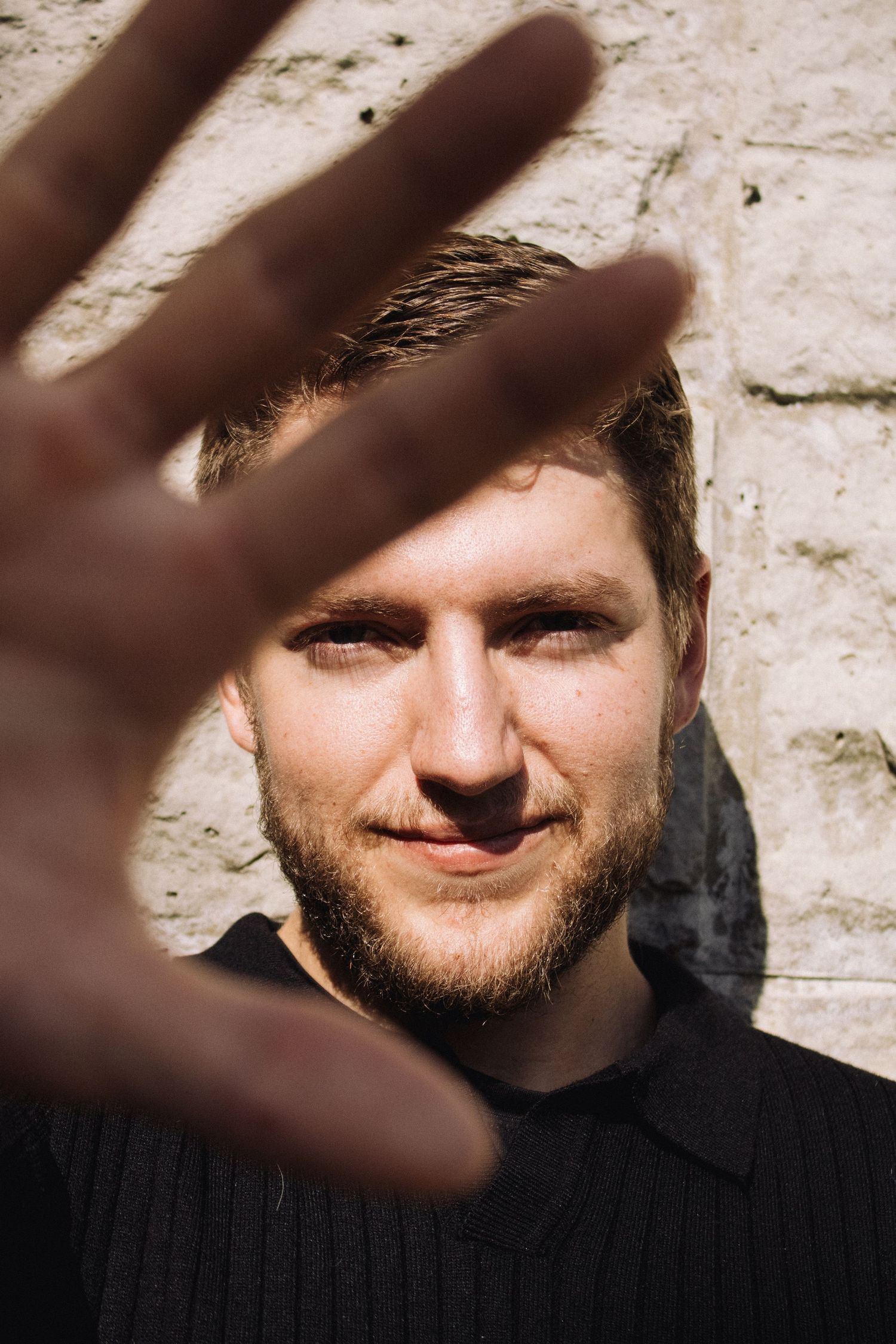 A hand reaches toward the camera casting a shadow over someone wearing a black sweater against a light colored wall.