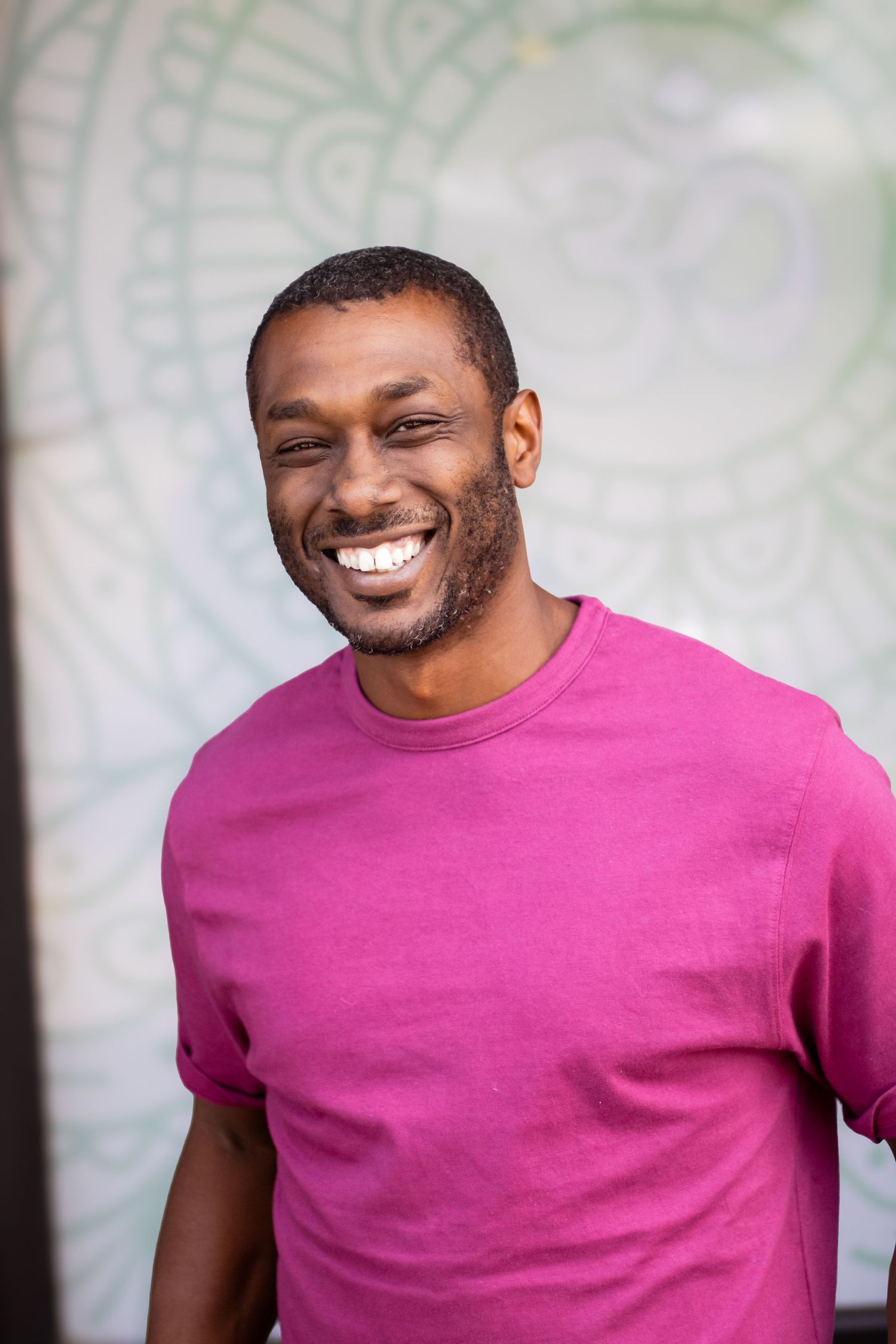 Person in bright pink t-shirt smiling warmly against a light colored wall.
