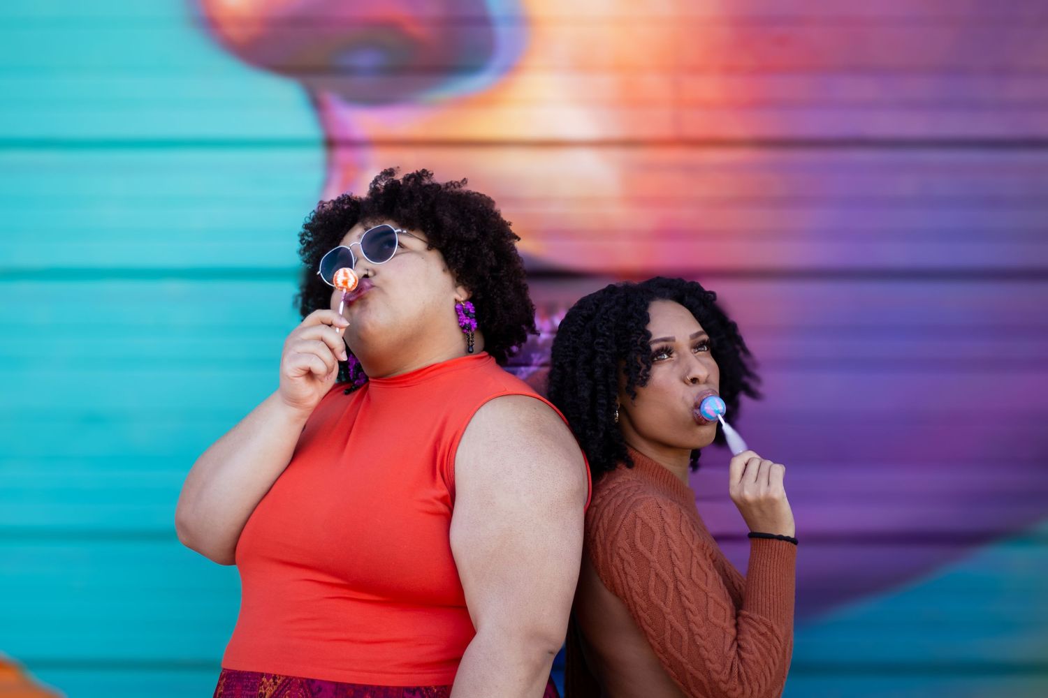 Two people in colorful outfits pose against a vibrant blue and purple gradient background in a photo series.