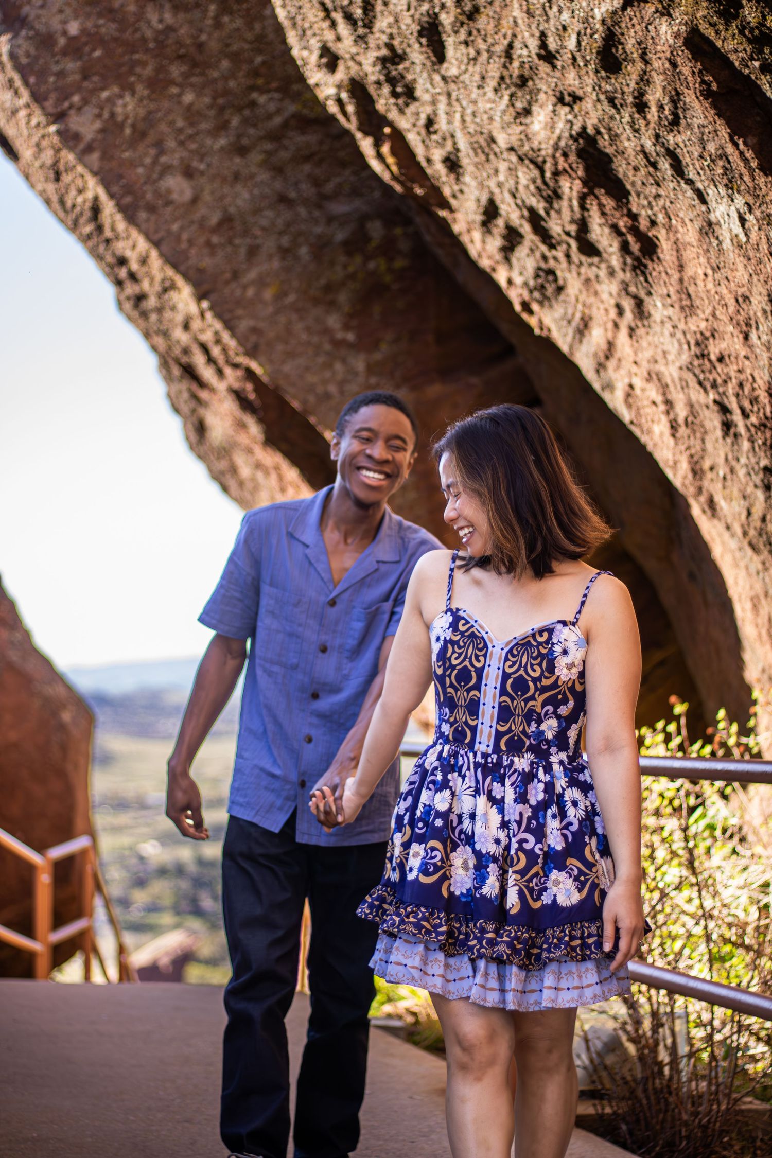 A couple shares joyful laughter together while standing on a scenic overlook with mountains in the background.