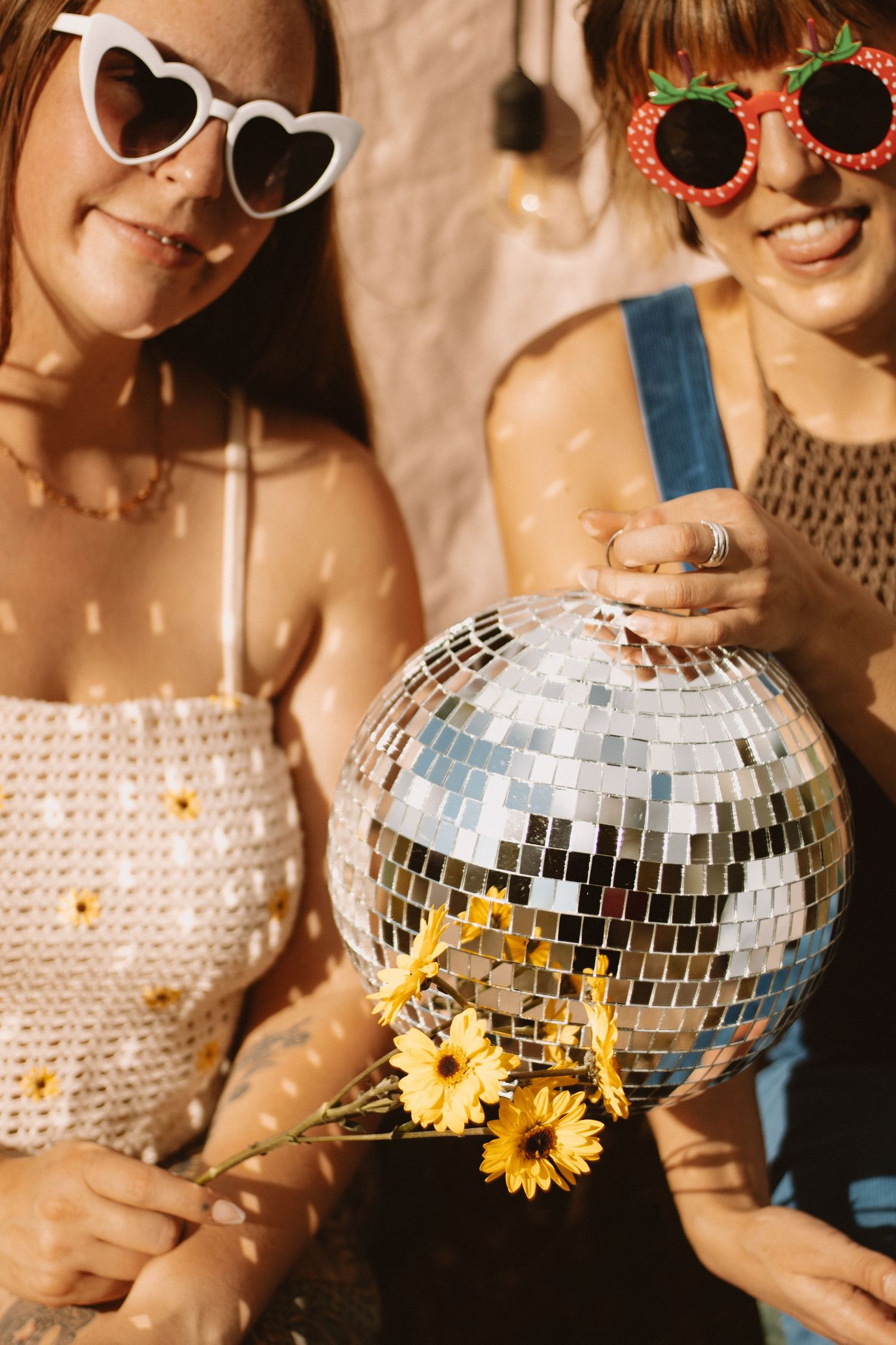 Group holding disco balls and wearing sunglasses pose with sunflowers in a warm-toned party setting.