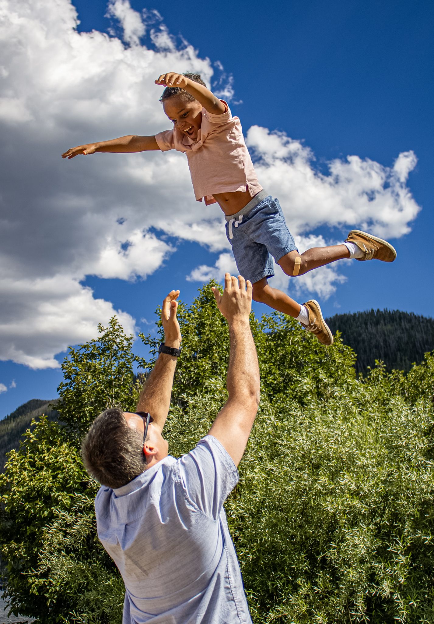 A sequence of joyful moments captured against a blue sky as a child is lifted and spun in a playful outdoor scene.