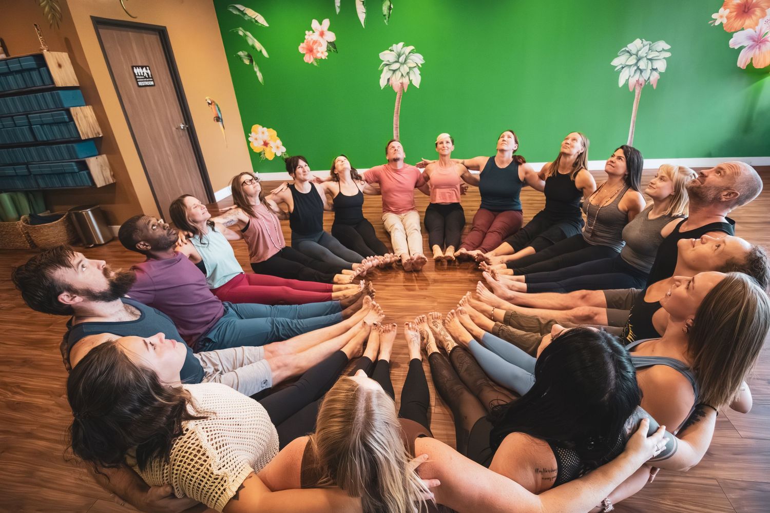 Students arranged in a circular pattern on floor during team building exercise in room with green walls.