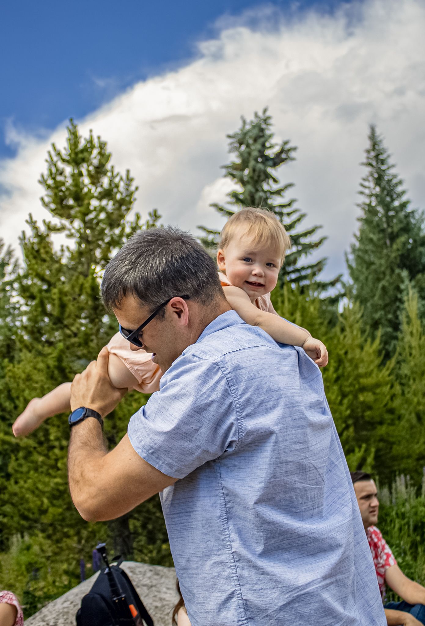 Playful outdoor sequence showing affectionate moments between family members against evergreen trees.