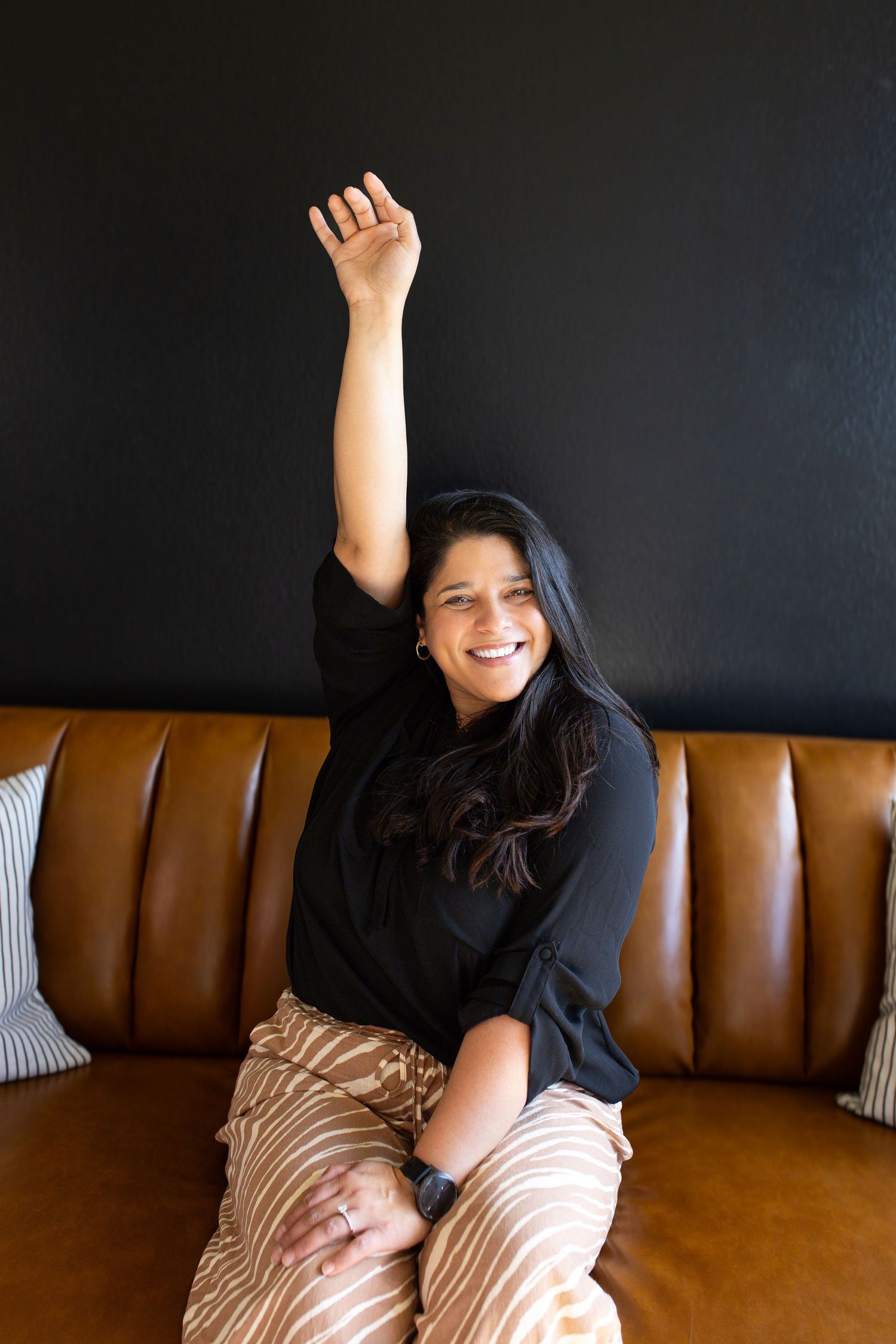 Person lounging playfully on brown leather couch against dark wall with decorative pillows.