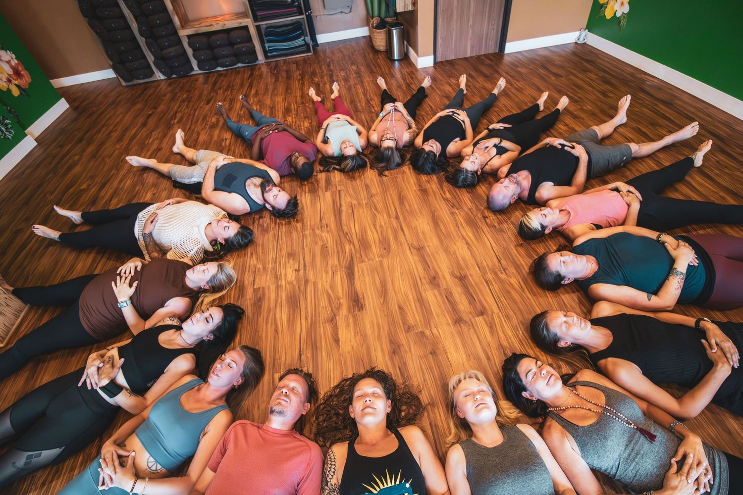 A group of people lying in a circle formation on a wooden floor creating a star-like pattern from above.