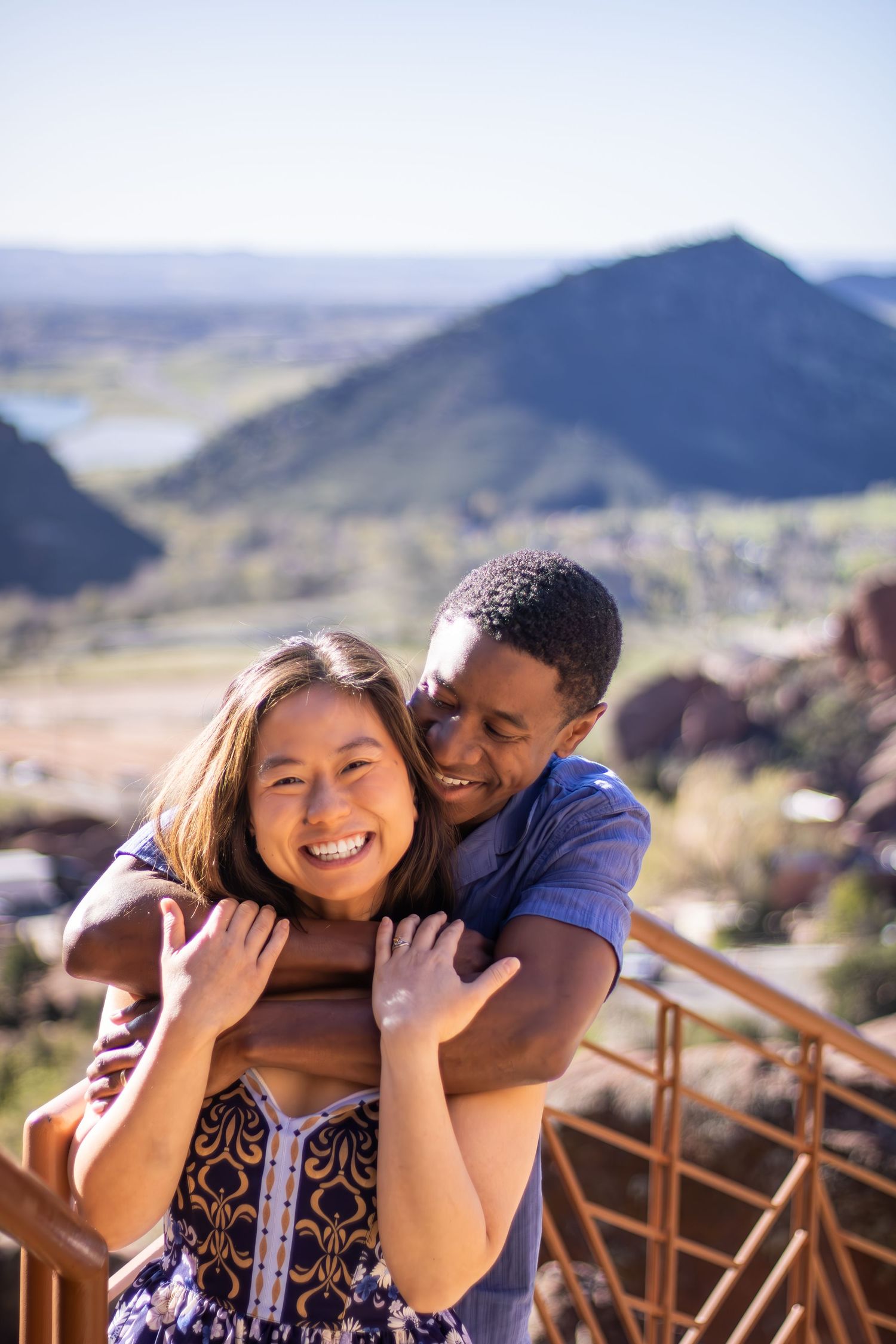 A happy couple shares a tender moment while enjoying scenic mountain views from a wooden deck overlook.
