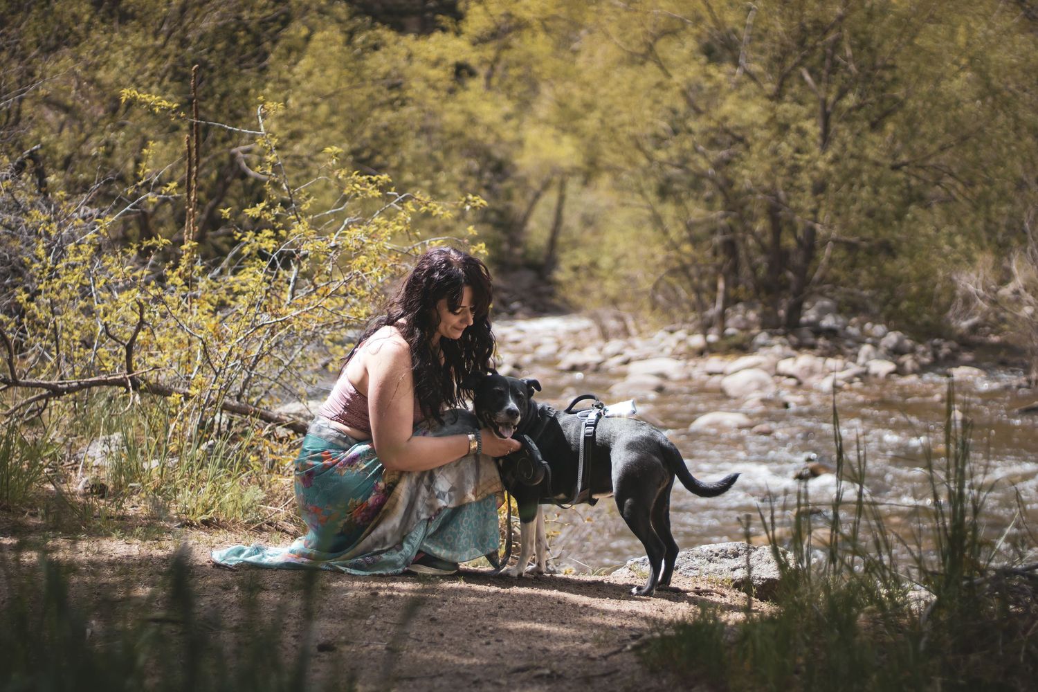 A couple sits together near a flowing stream in a scenic outdoor setting during autumn.