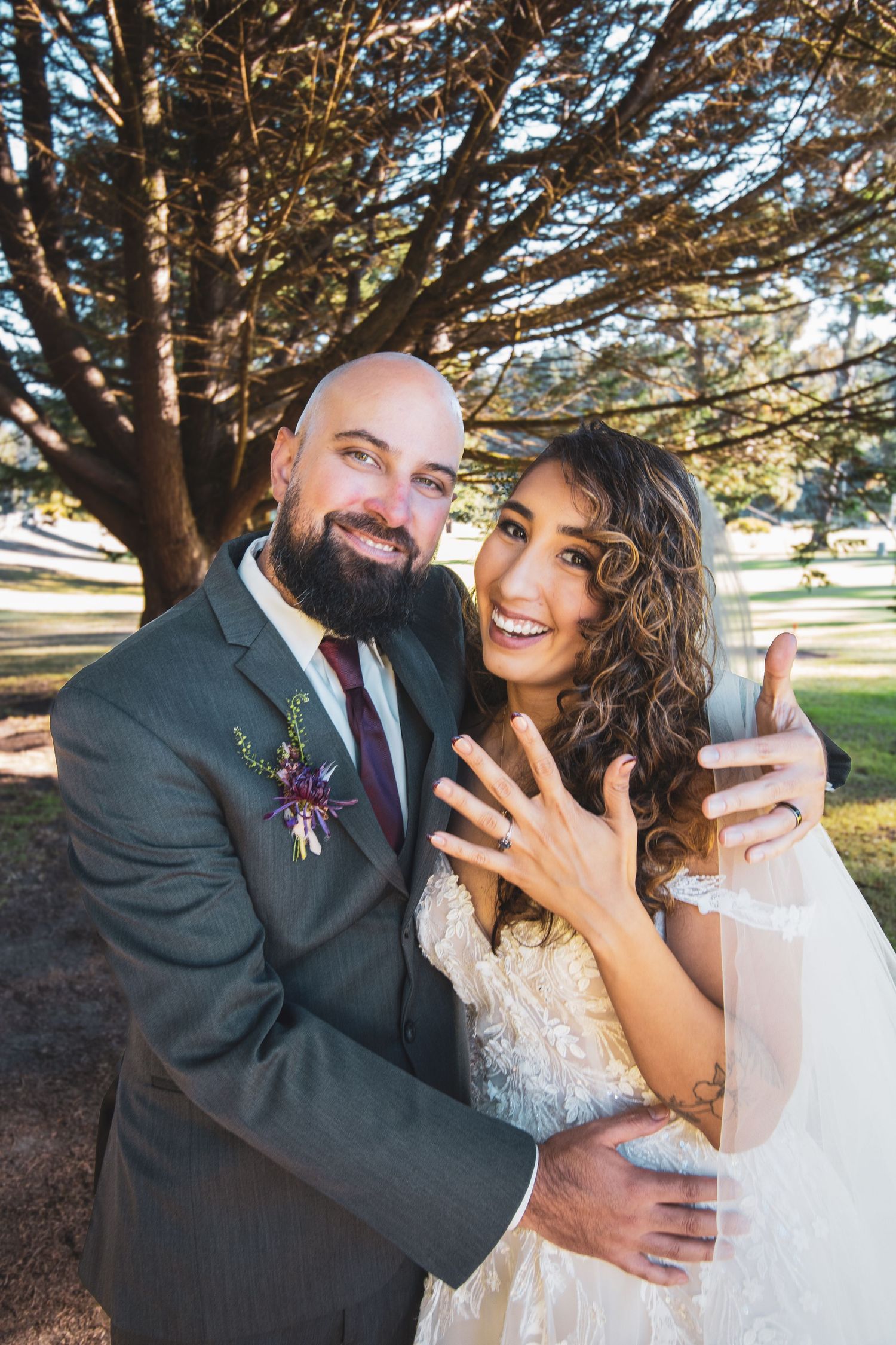 A joyful couple shares intimate moments under a large tree during their wedding photo session.