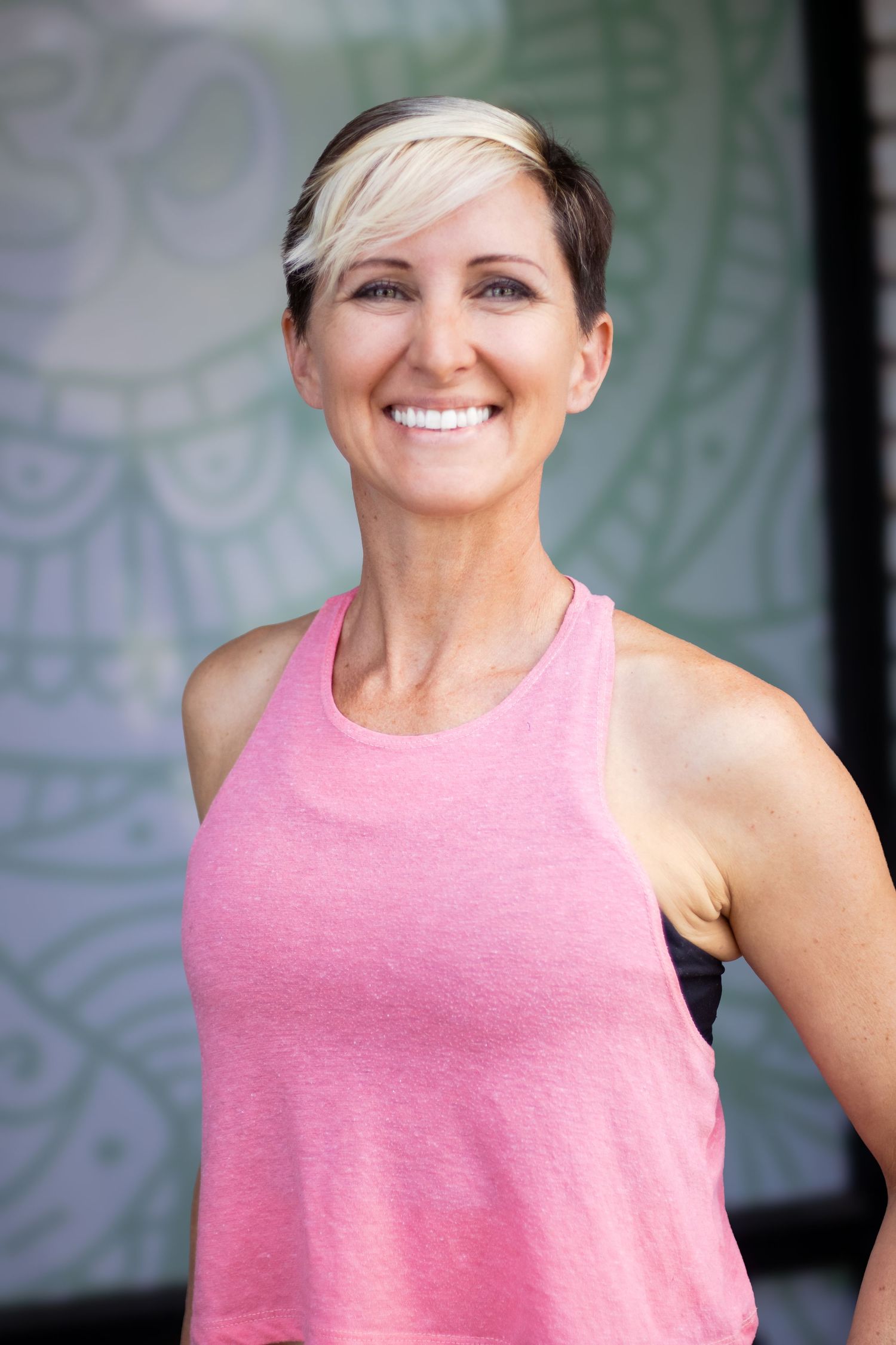 Woman in pink athletic tank top smiling against light colored background.