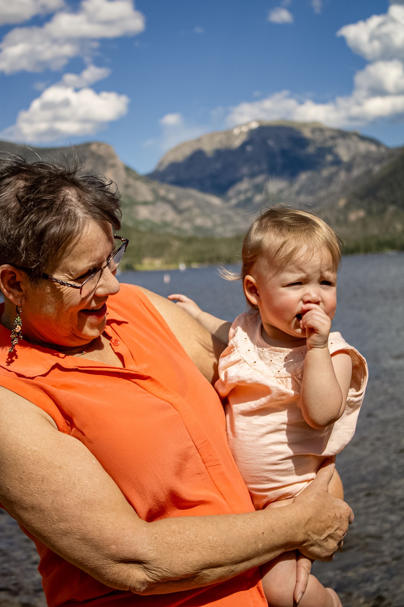 Two people share a tender moment while sitting by a scenic mountain lake on a sunny day.