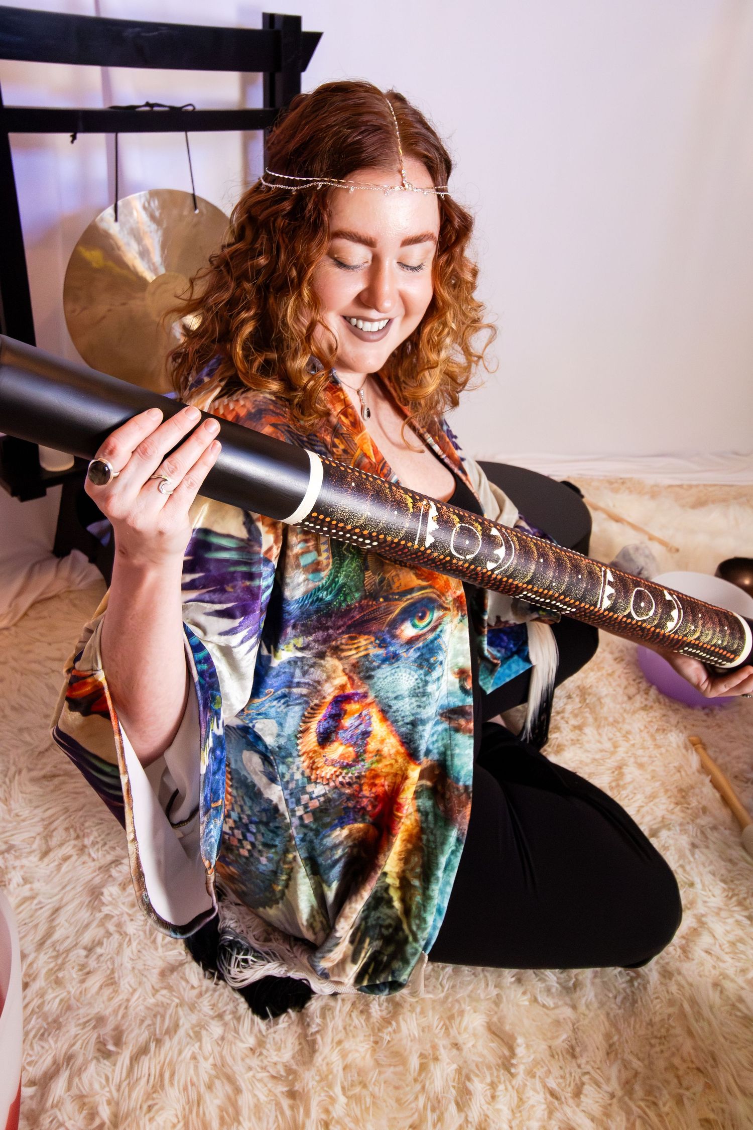 A person with red curly hair lies on a cream carpet playing an electric guitar in a colorful galaxy print shirt.