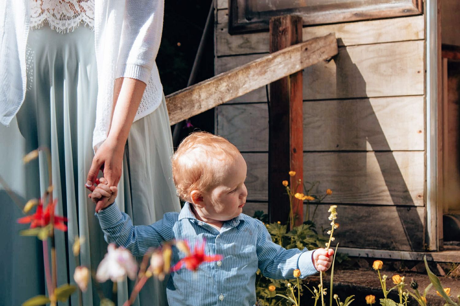 A child plays outdoors in a rustic wooden setting with colorful flowers in the background.