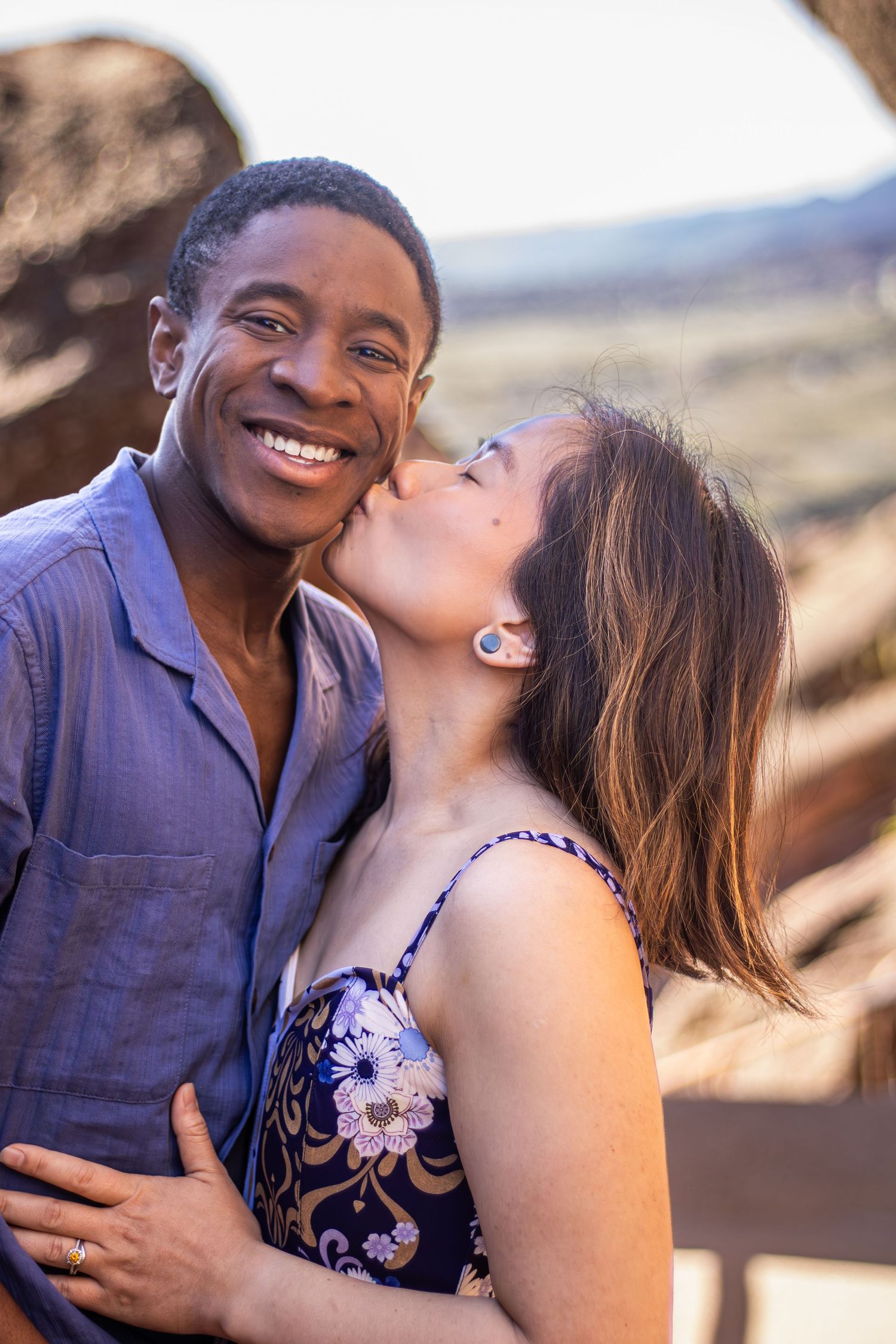 A joyful couple shares an intimate moment against a desert mountain backdrop on a sunny afternoon.