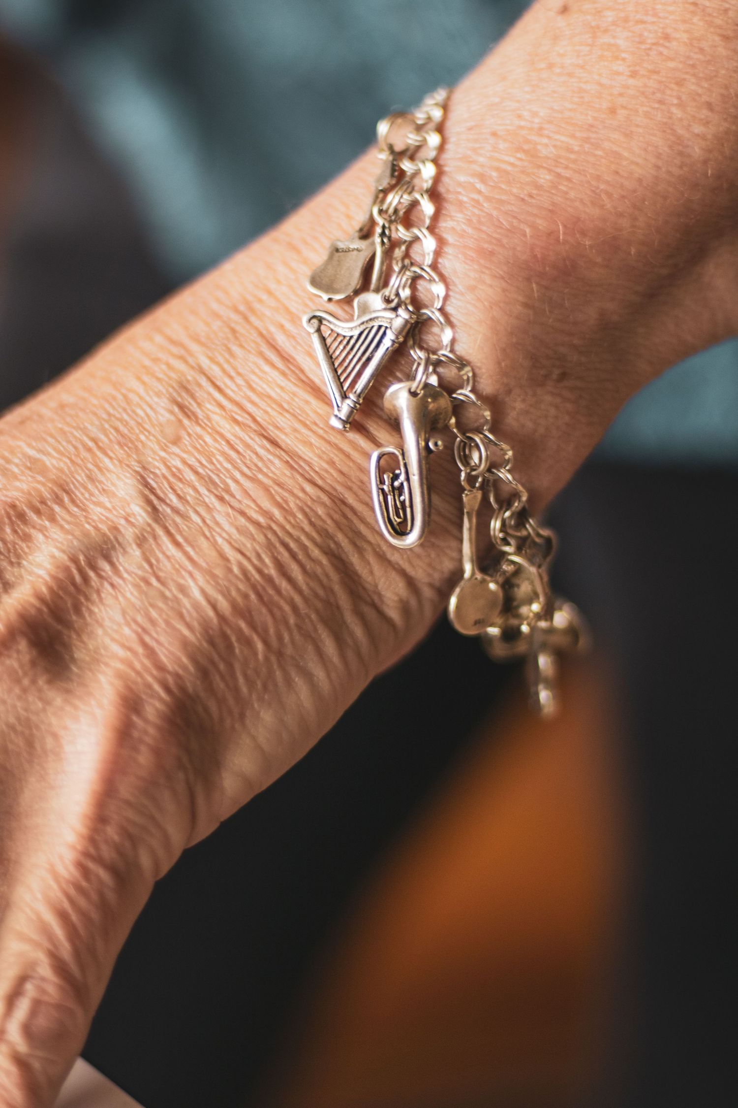 A silver charm bracelet with musical instrument charms and hearts worn on a person's wrist.