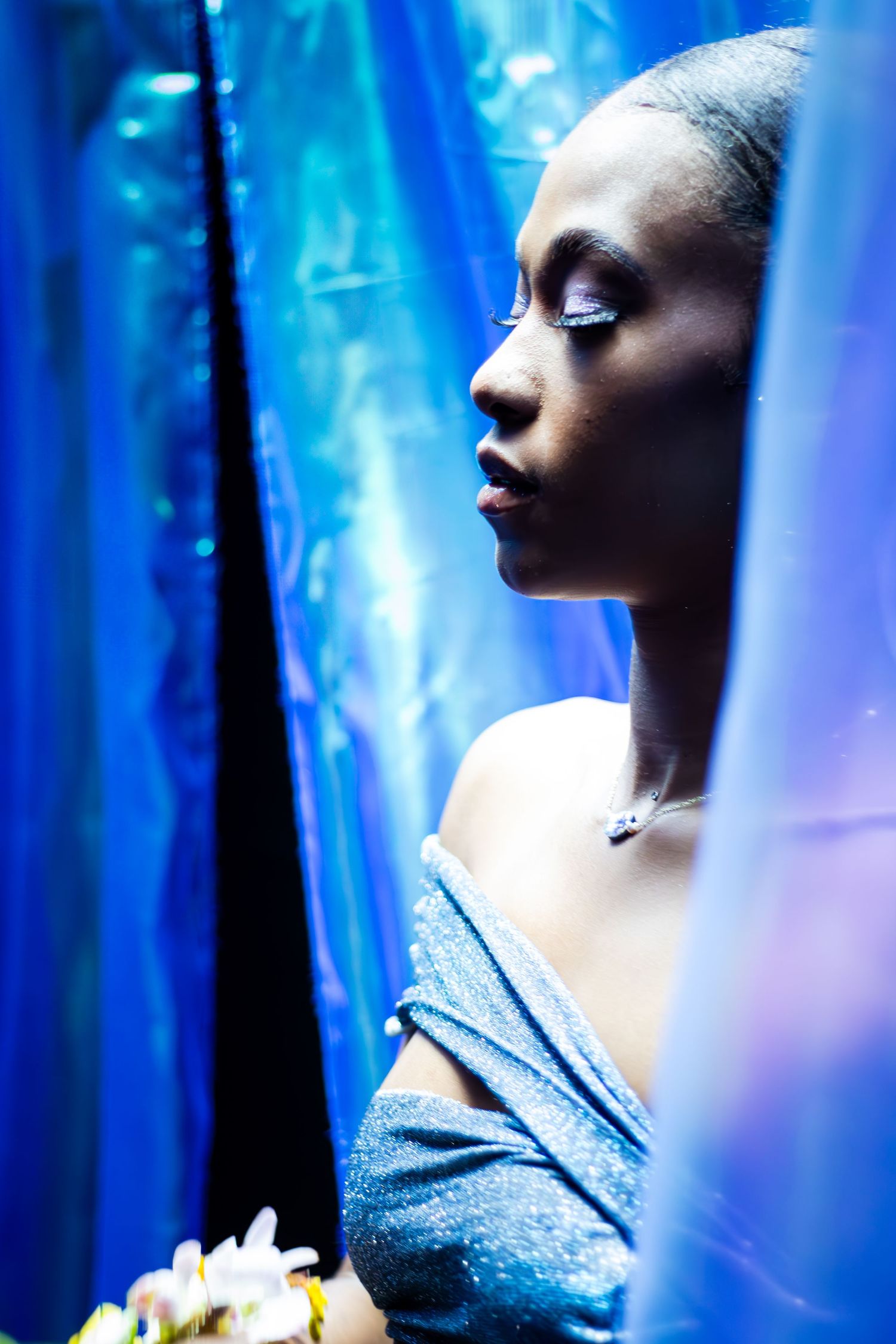 Artistic portrait with blue lighting shows a serene profile against ethereal fabric and floral elements.
