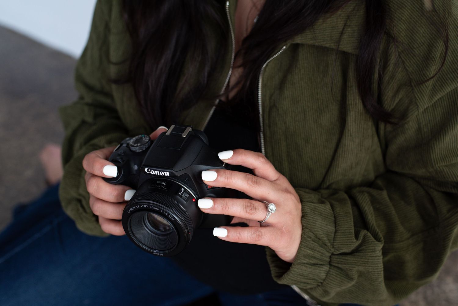 A person wearing an olive green jacket holds and examines a black DSLR camera.