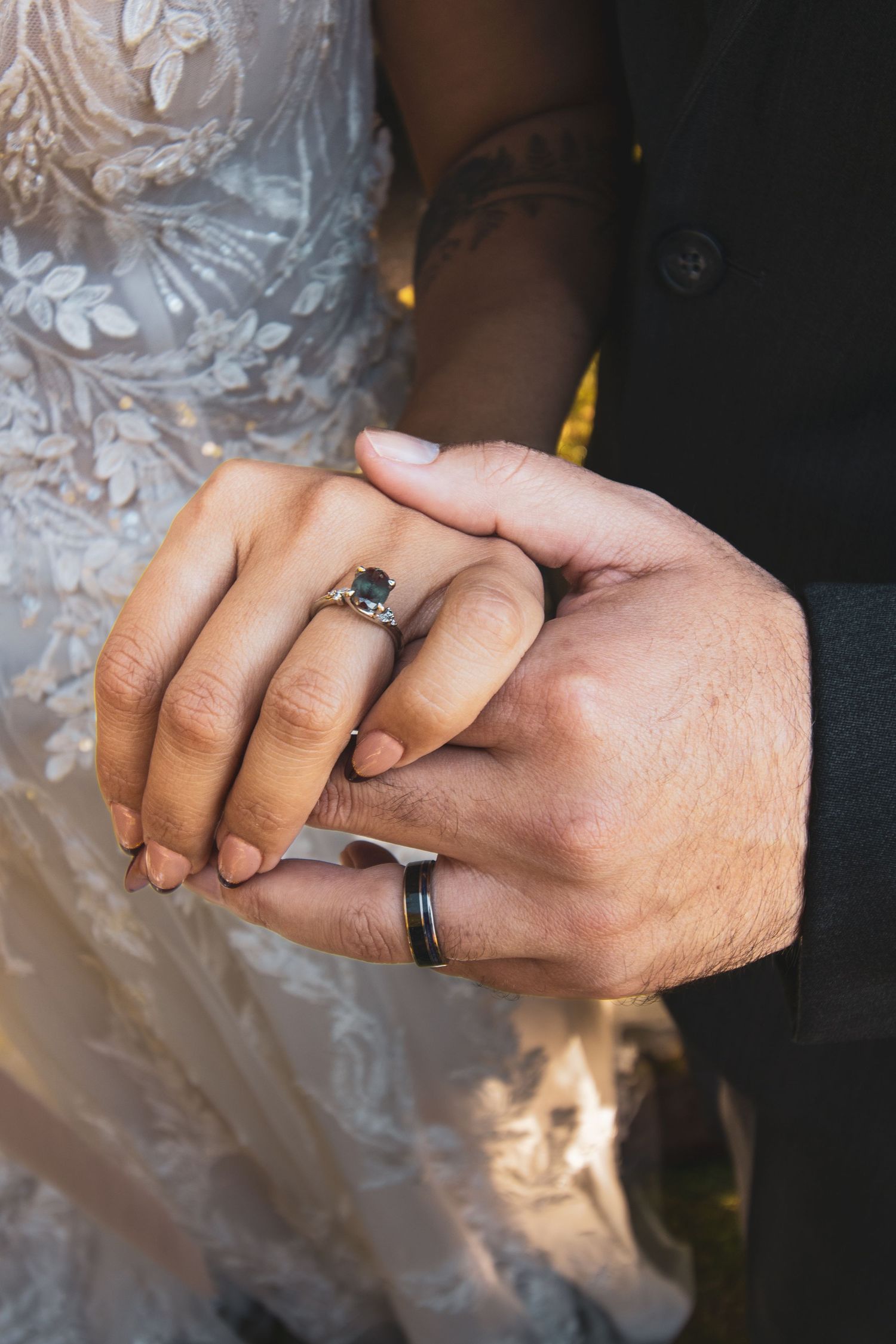 Close-up shot of two hands wearing wedding rings against a white lace dress background.