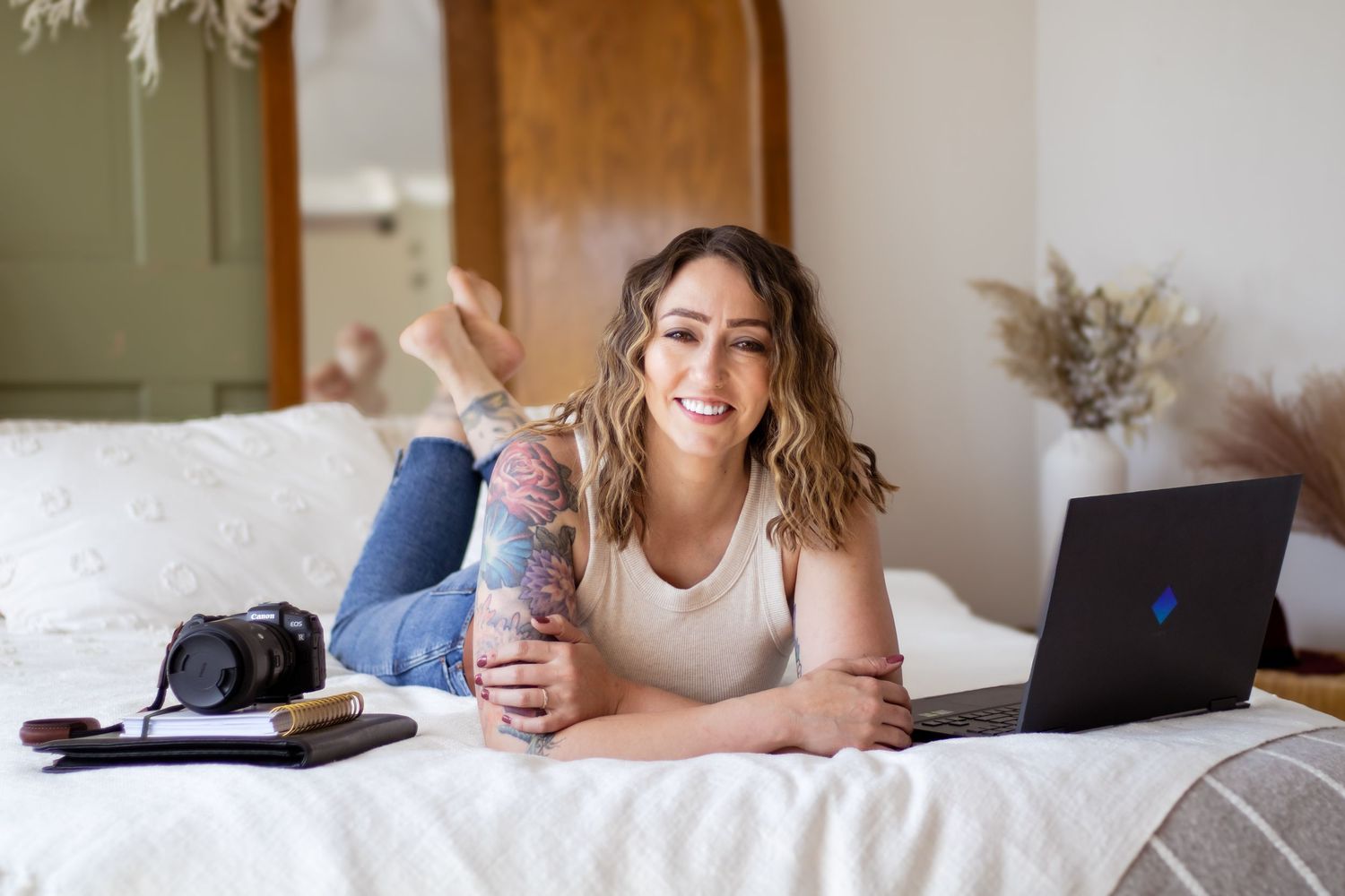 A person relaxes on a cozy white bed with a laptop while working from home.