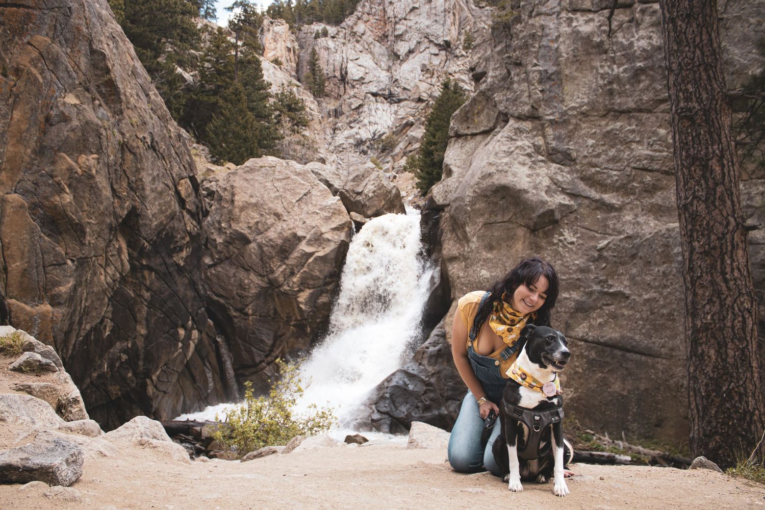 A scenic waterfall cascades down rocky cliffs in a mountain forest setting with hikers exploring the natural landscape.