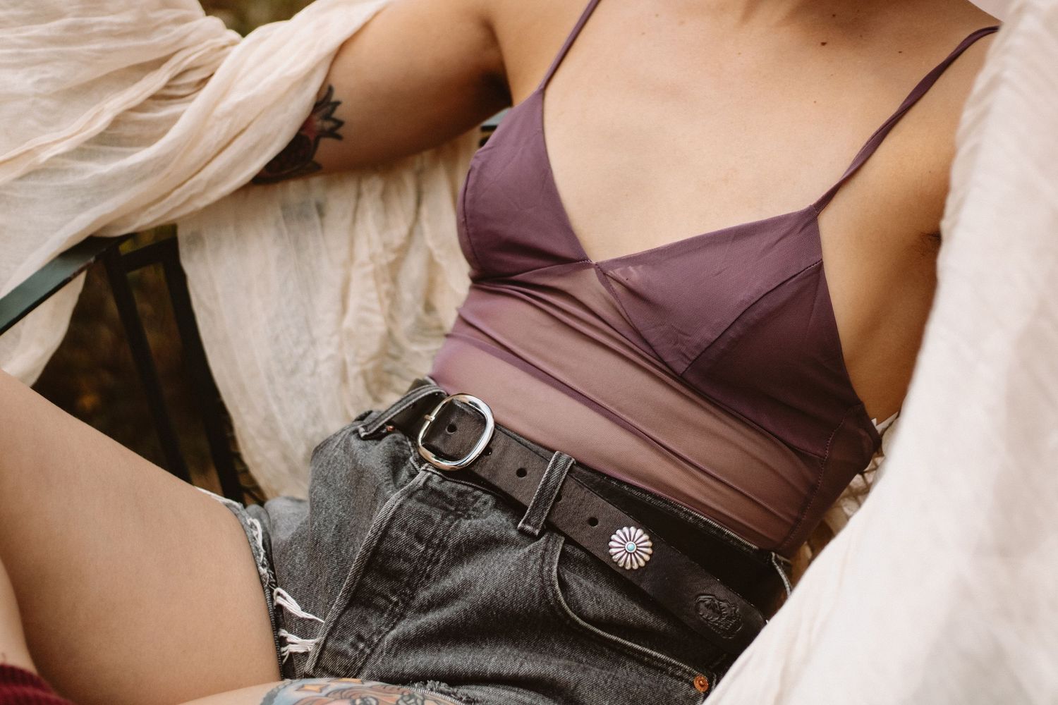 Close-up fashion detail of mauve crop top and high-waisted denim jeans with silver belt buckle.