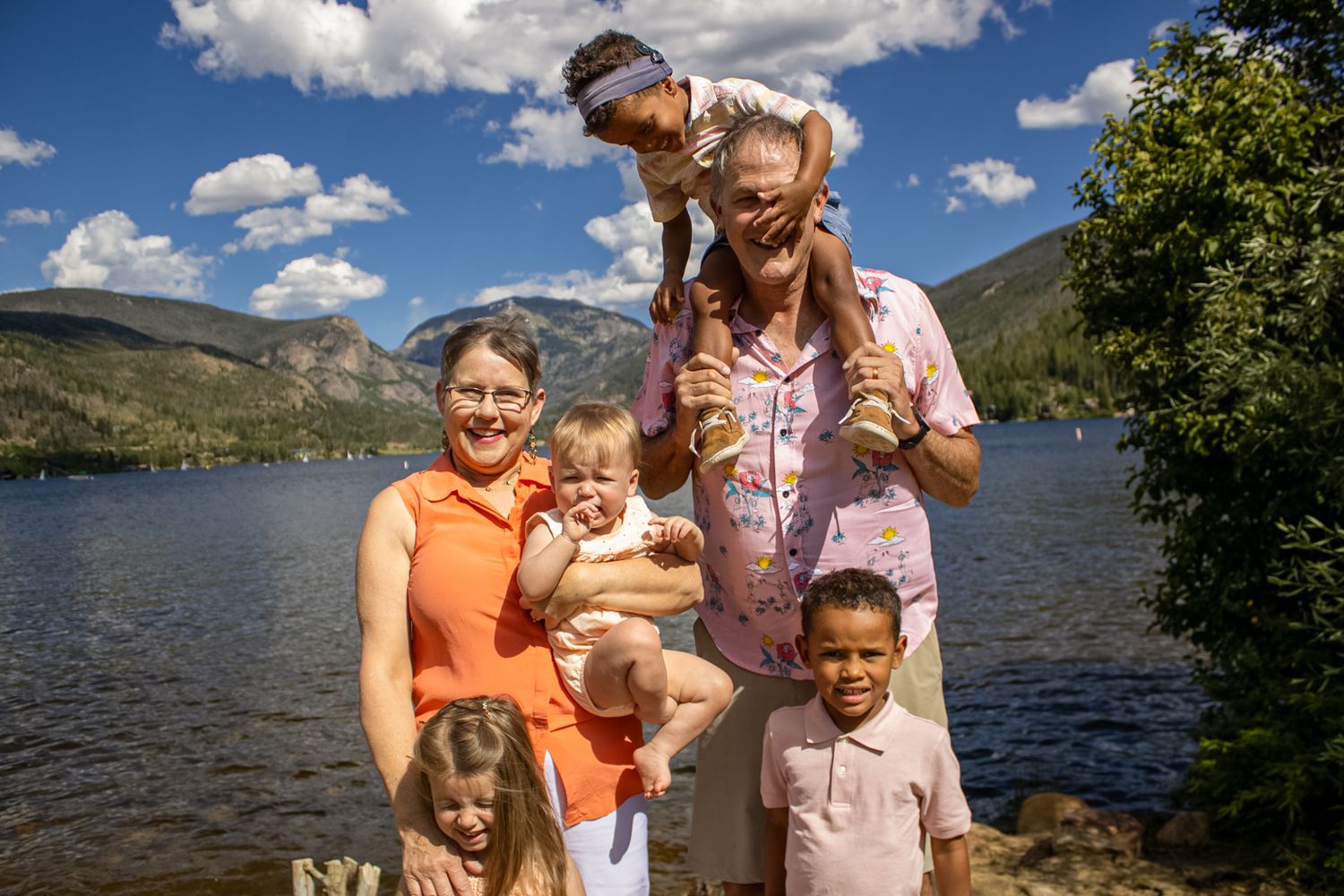 A group enjoying a sunny day by a scenic mountain lake with blue skies and puffy clouds in the background.