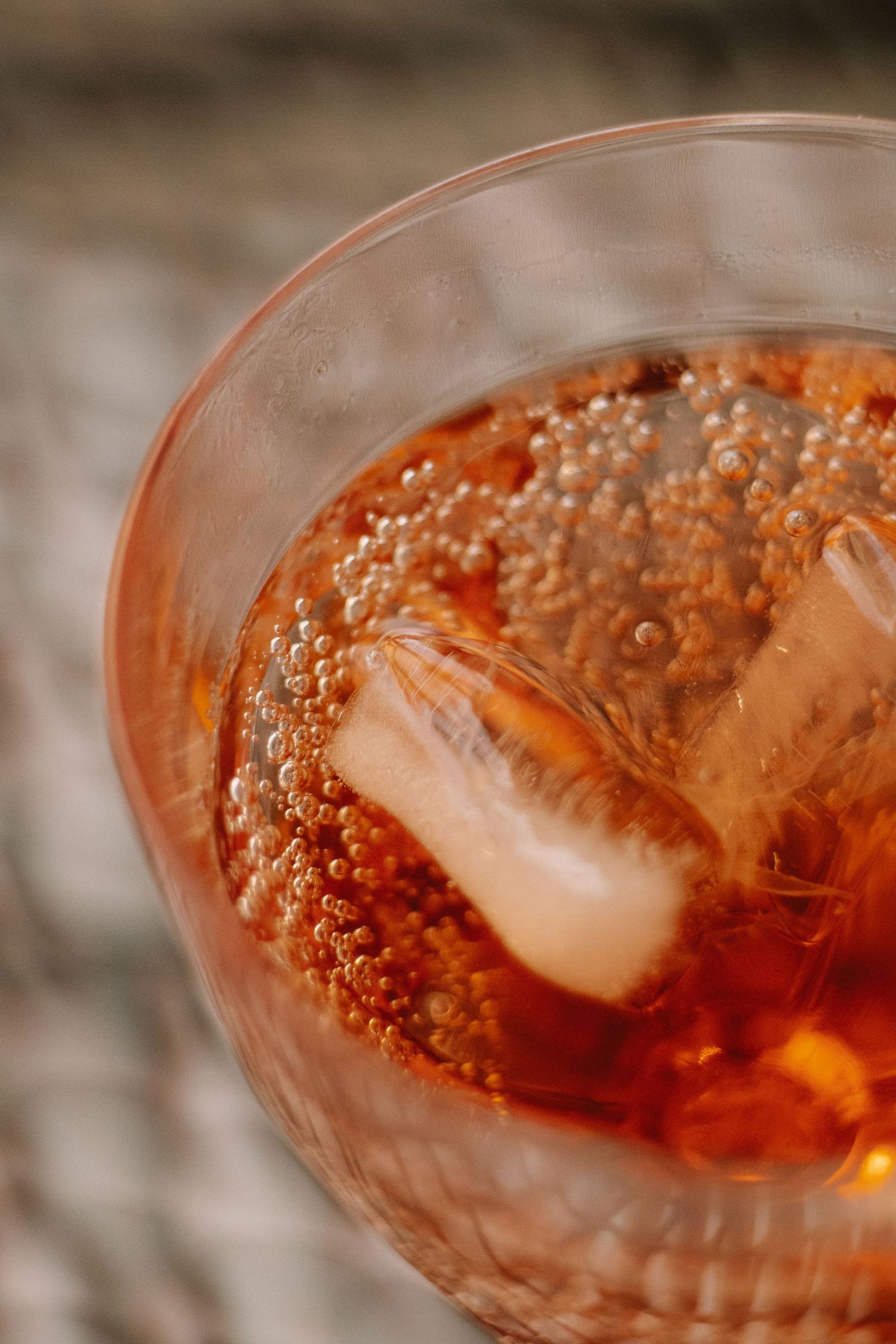 Close-up view of a sparkling rose cocktail with ice cubes in a glass showing bubbles and warm amber hues.