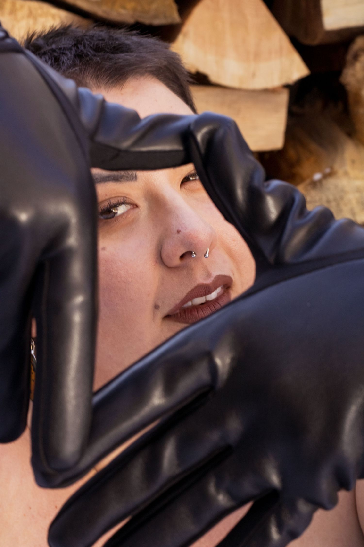 Close up artistic portrait with black latex gloves framing the subject against stacked firewood background.